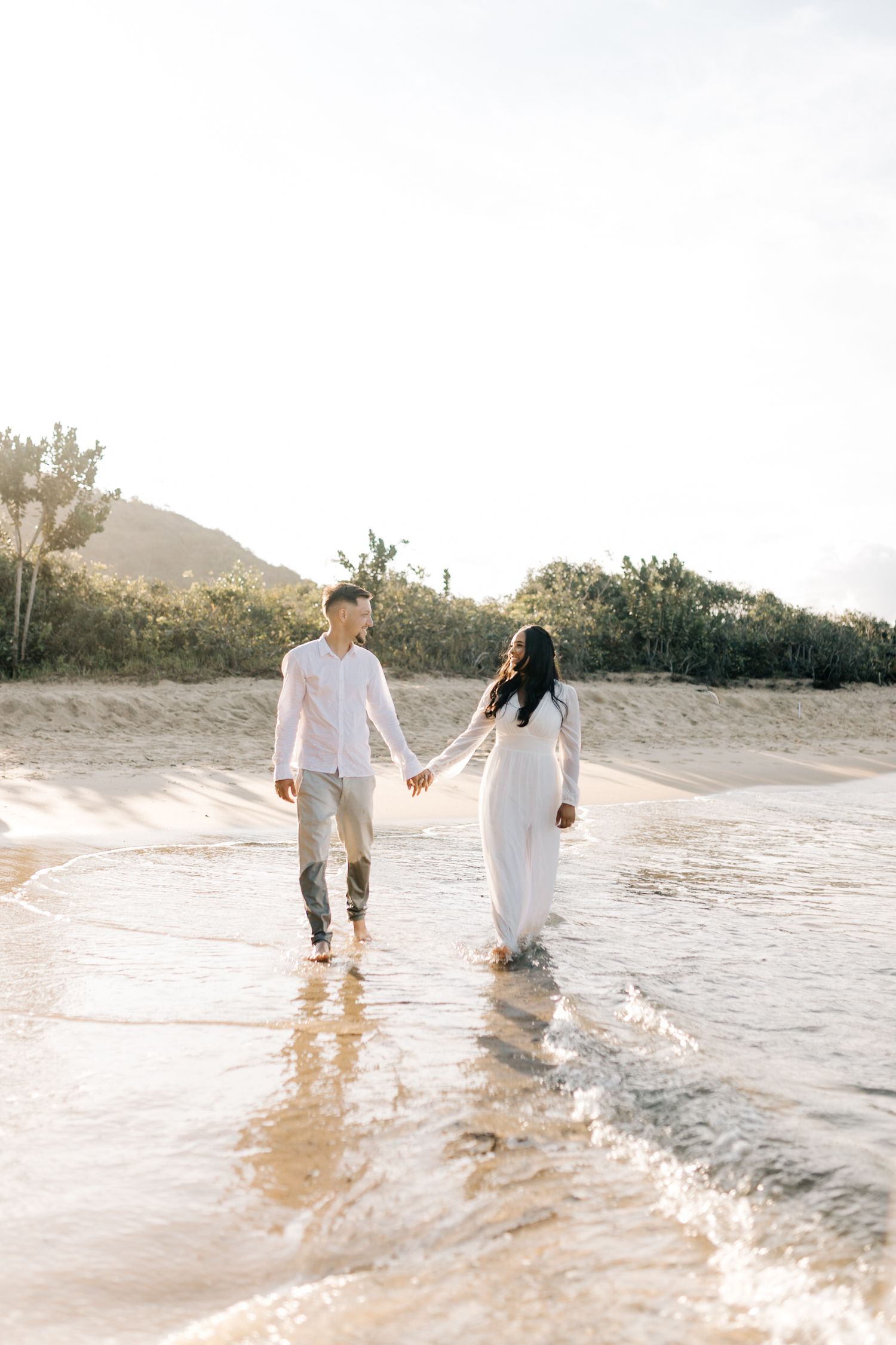 A couple takes a romantic beach walk holding hands while waves lap at their feet.