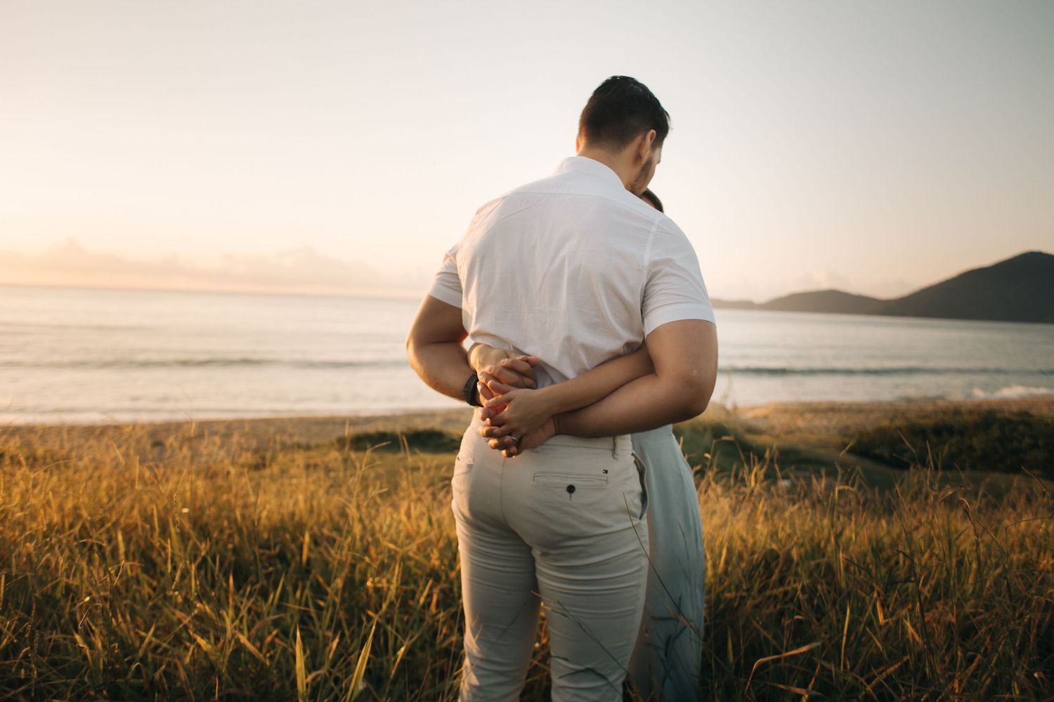Couple in casual white outfits enjoying sunset views along the coastline.
