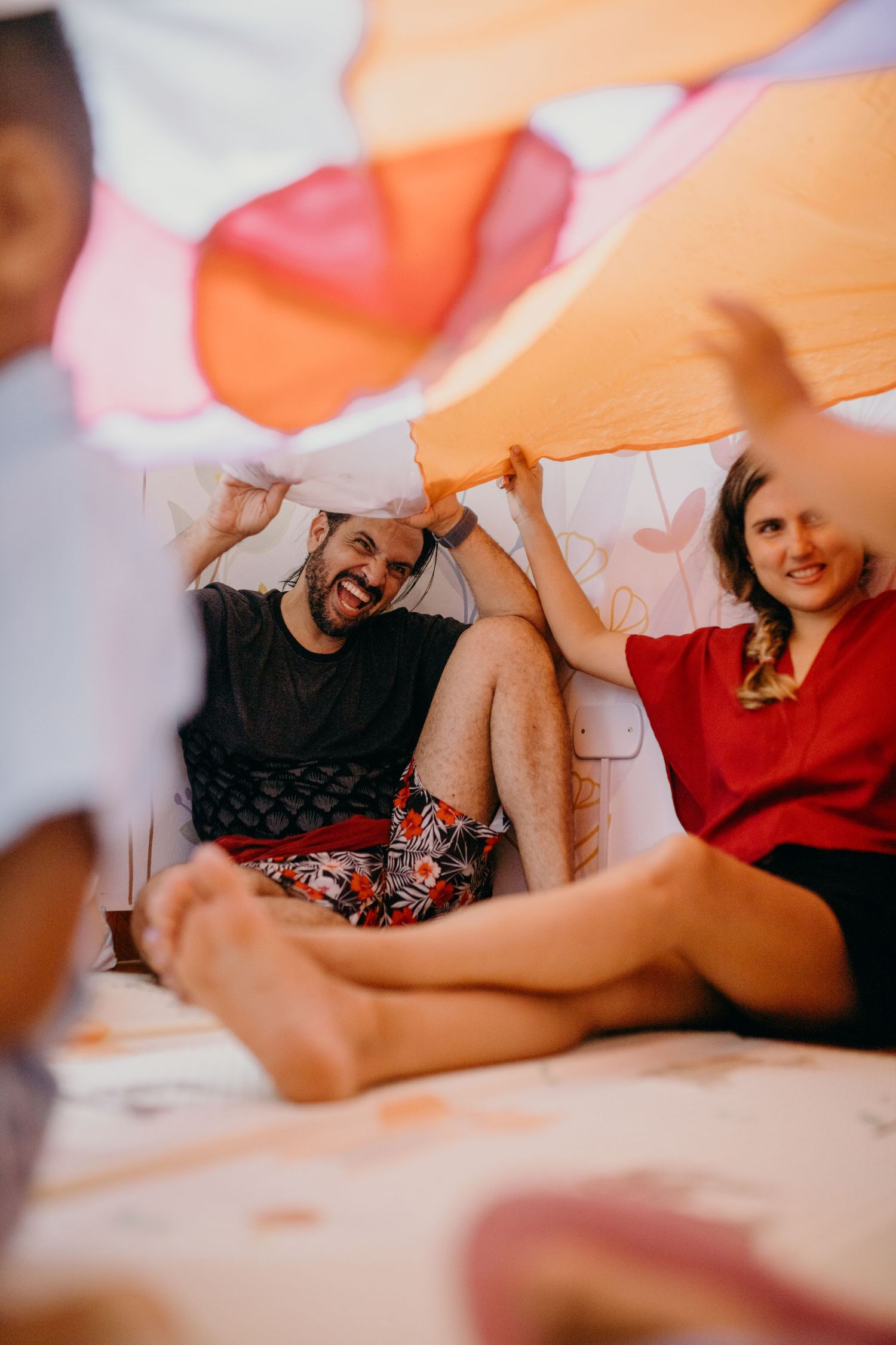 People relaxing under a colorful blanket fort made of orange and pink fabrics.