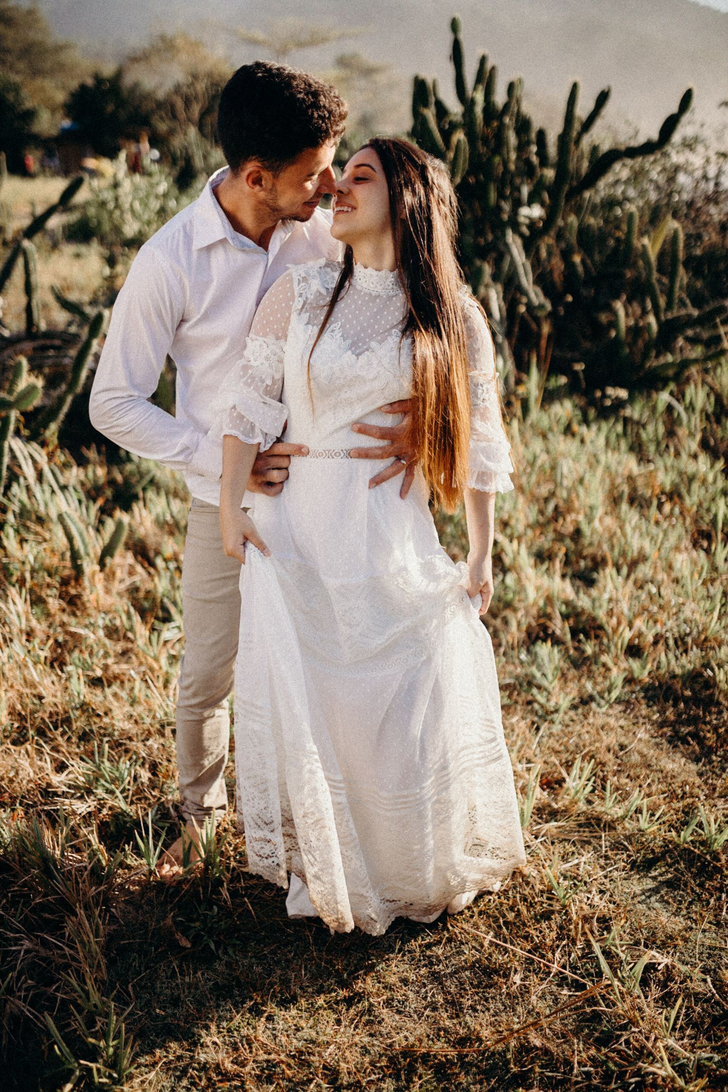 A couple shares an intimate moment among desert cacti during a golden hour photoshoot.