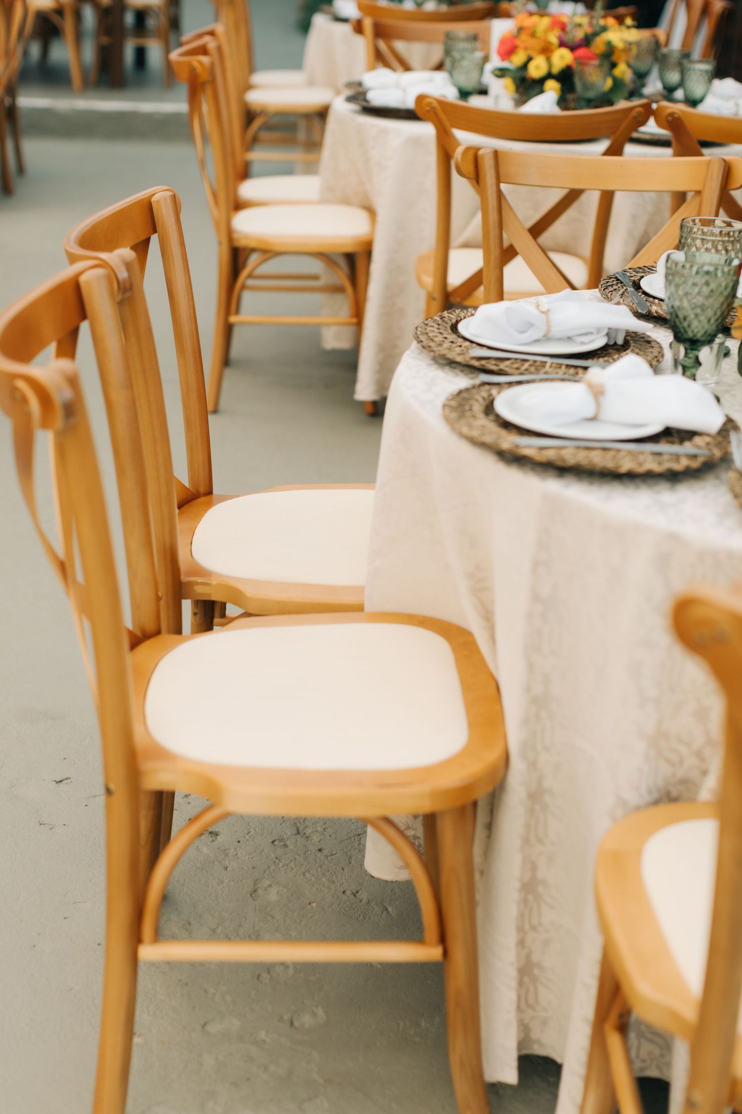 Elegant wedding reception table settings with wooden chairs and white linens.