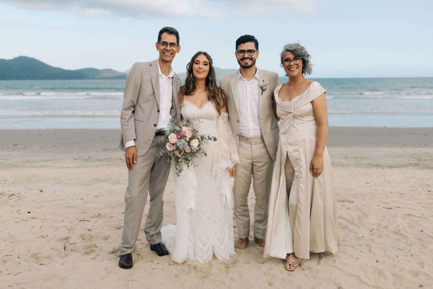 Beachside wedding party in neutral tones gathers for formal portrait with ocean view.