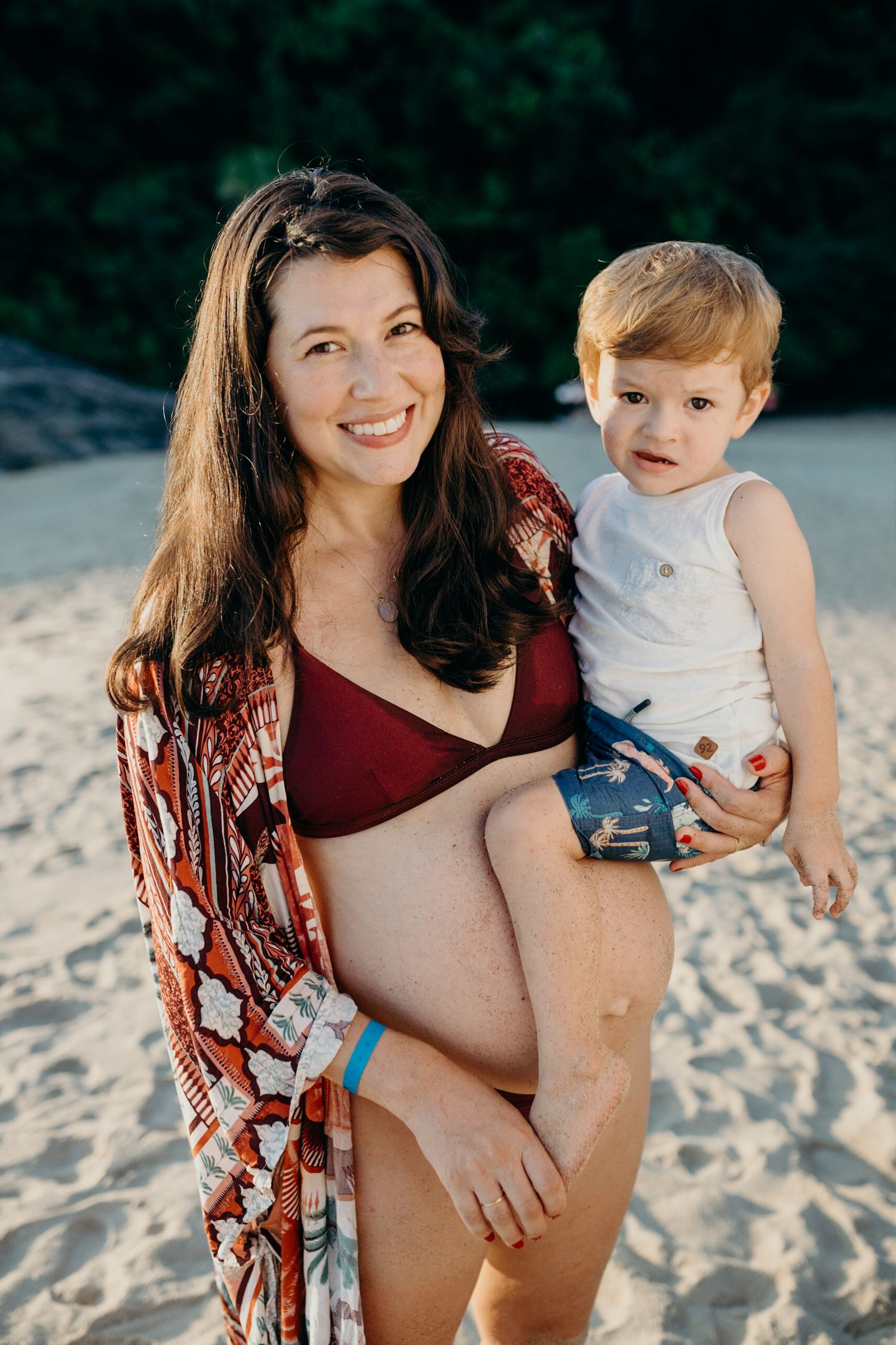Expectant mother poses with family on beach during sunset photo session.