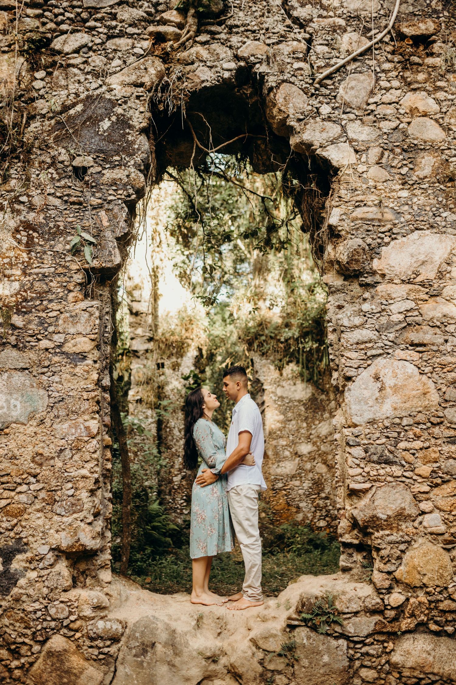 A couple stands intimately in an ancient stone doorway surrounded by moss and ruins.