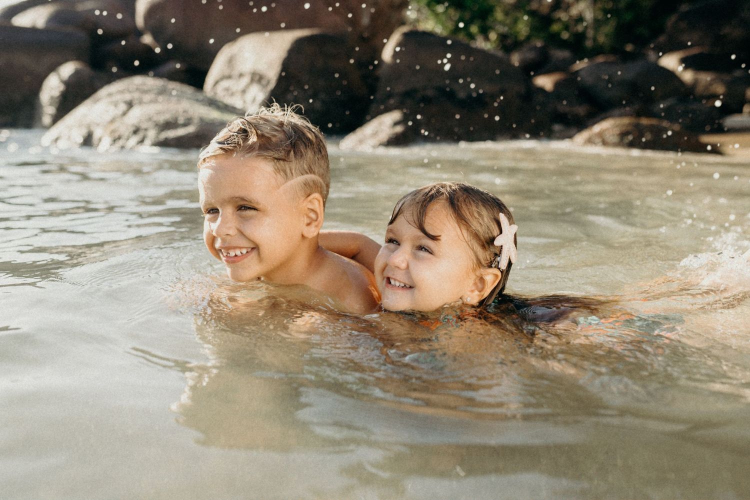 Two children splashing and laughing in ocean water during a sunny beach day.