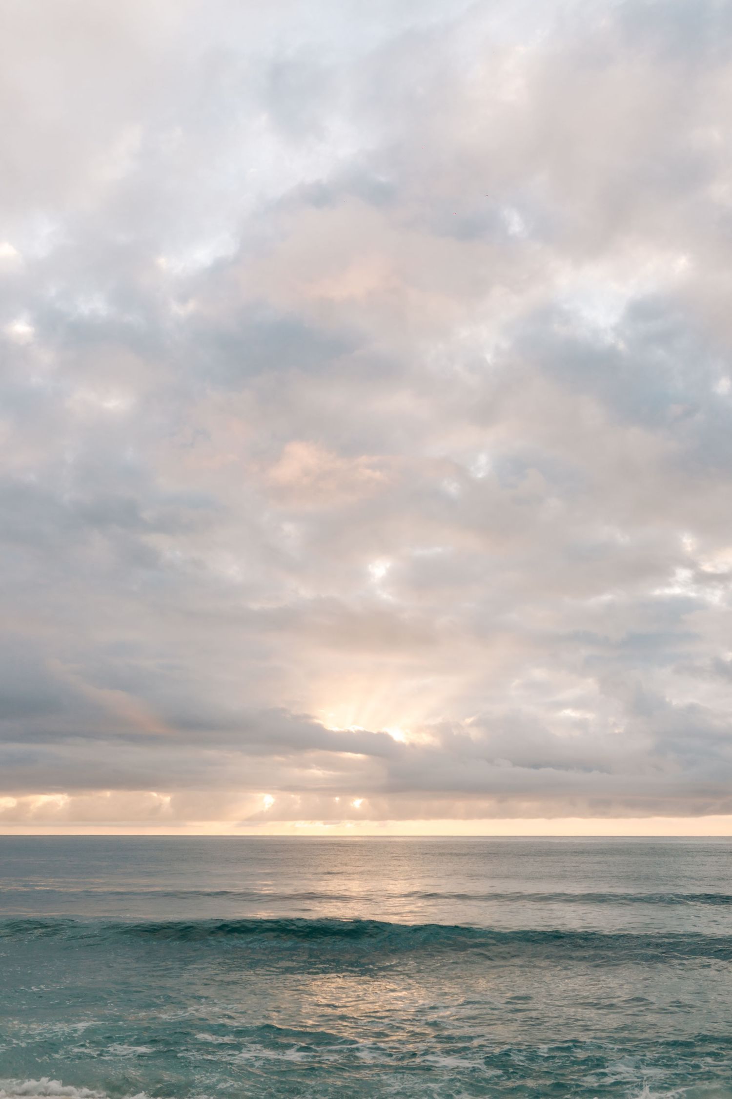 Dramatic cloudy sunset over turquoise ocean waters with gentle waves.