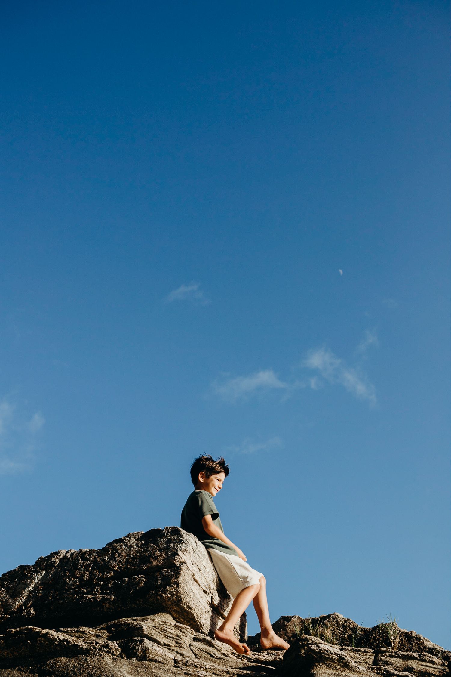 Silhouette of person sitting on rocky cliff against vibrant blue sky.