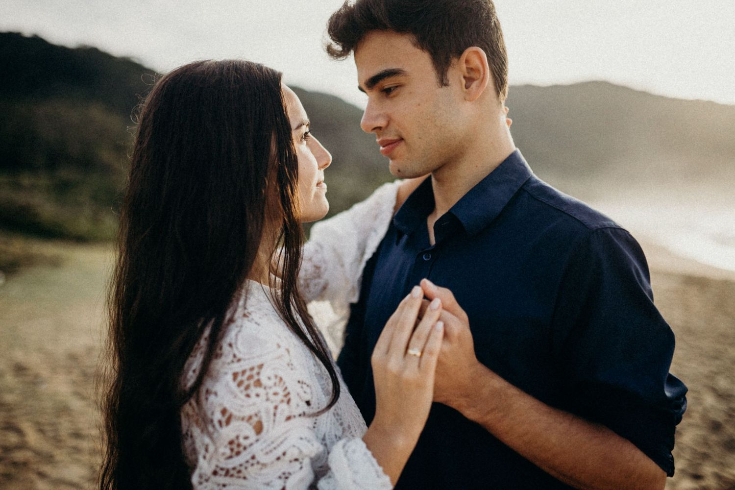 A couple stands together in sunlit golden hills during their engagement photography session.