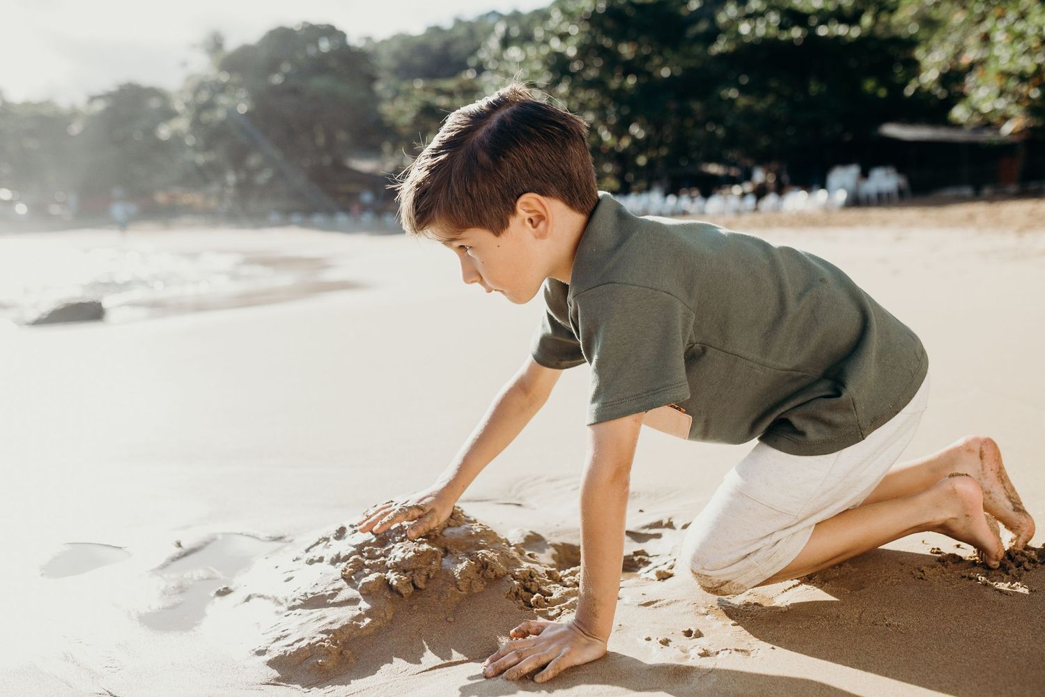 Young child plays in the sand at the beach during golden hour.