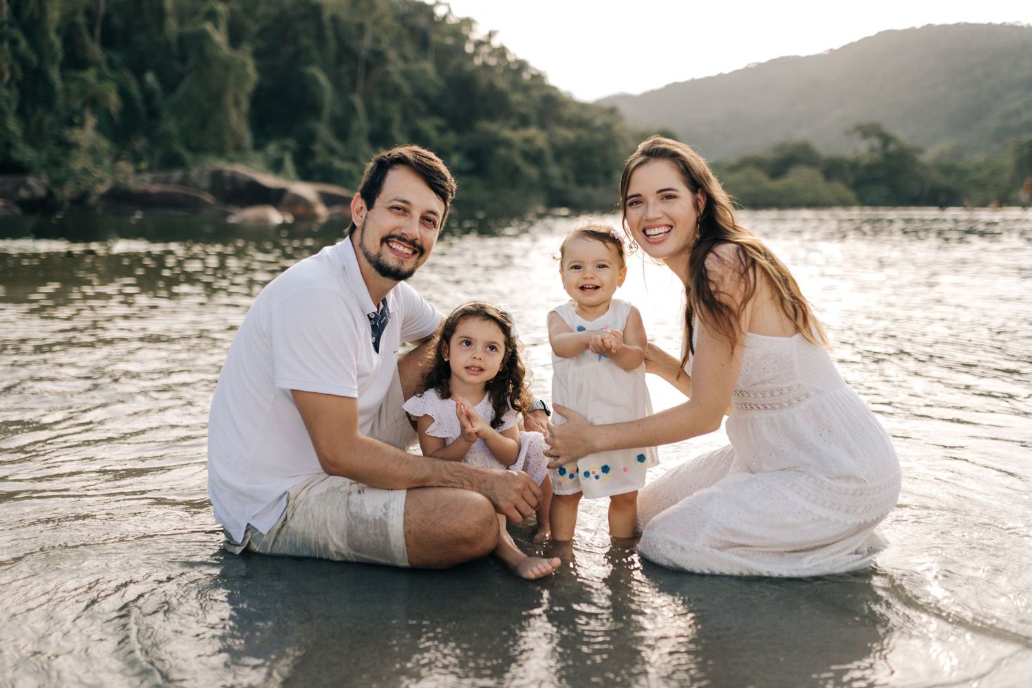 A happy family moment captured by the lake with everyone dressed in matching white outfits.