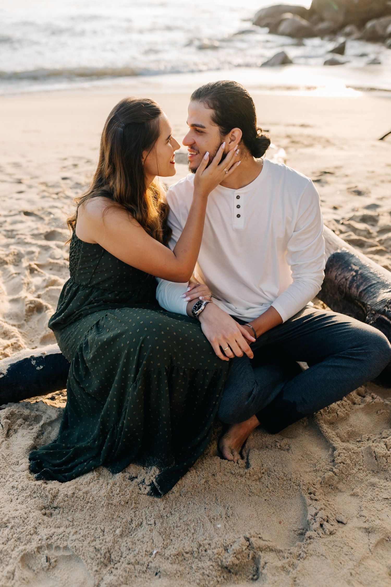 Intimate moment between couple sitting on sandy beach at sunset.