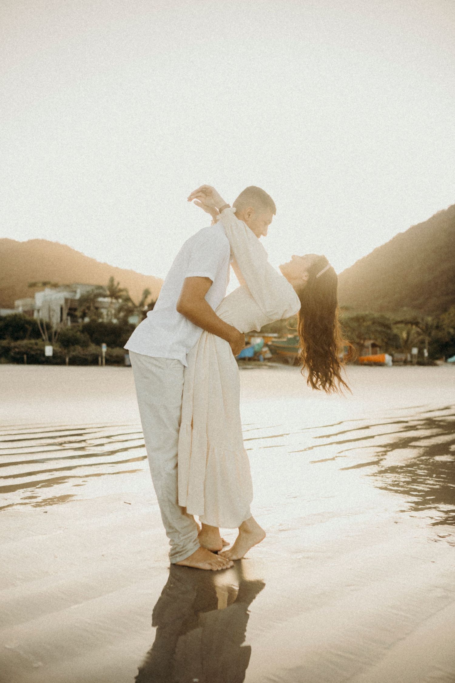 Romantic couple pose playfully on beach during golden hour.