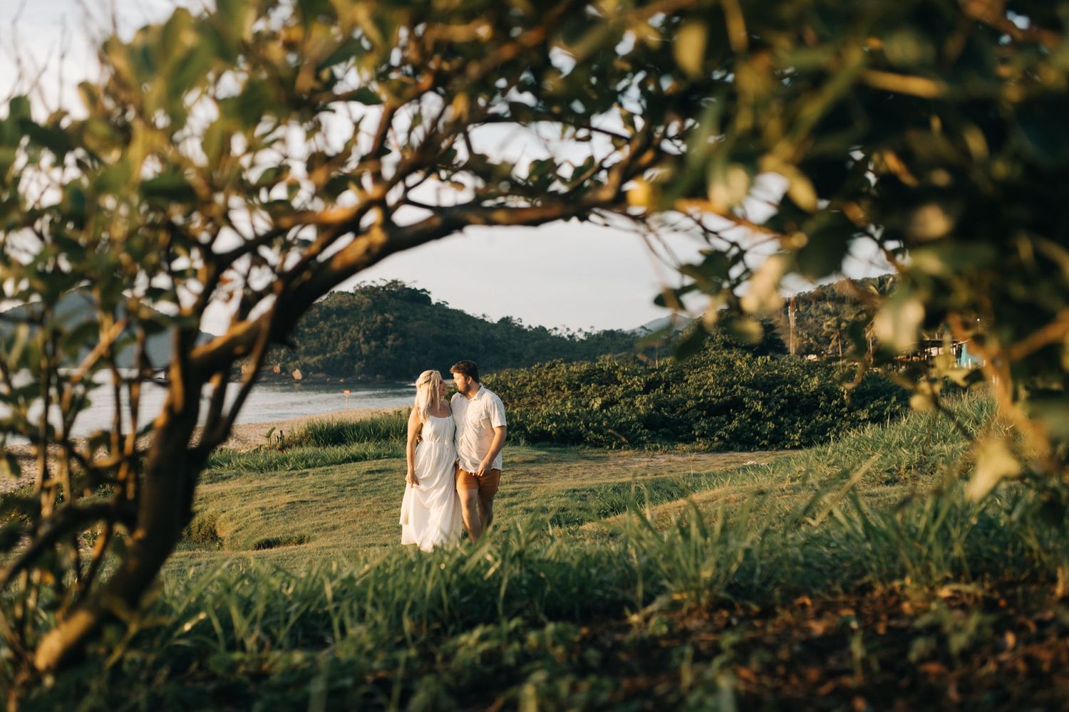 A couple stands together on a hilltop overlooking mountains and valleys in warm sunlight.
