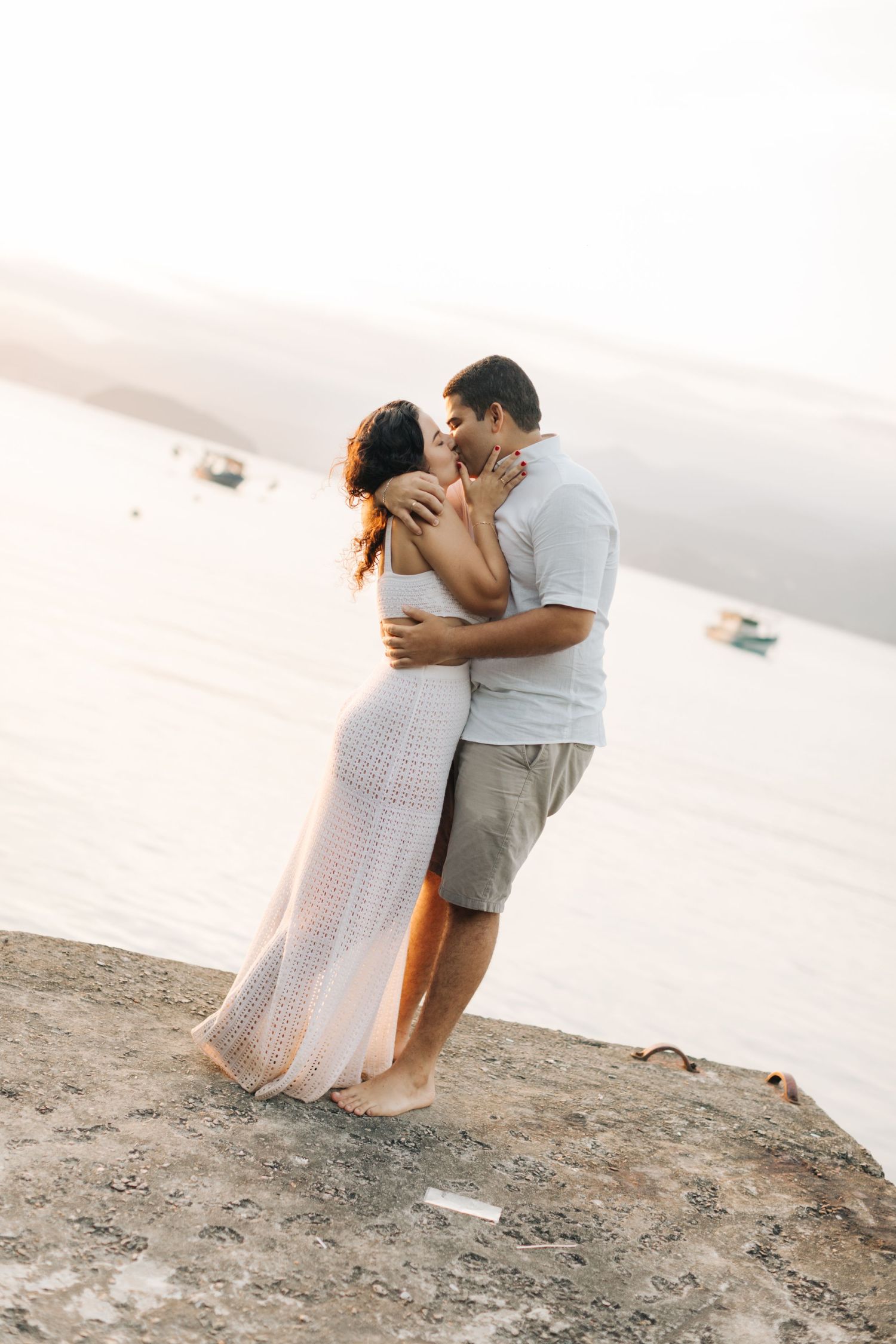 A romantic couple shares an intimate moment on a cliff overlooking a serene lake at golden hour.