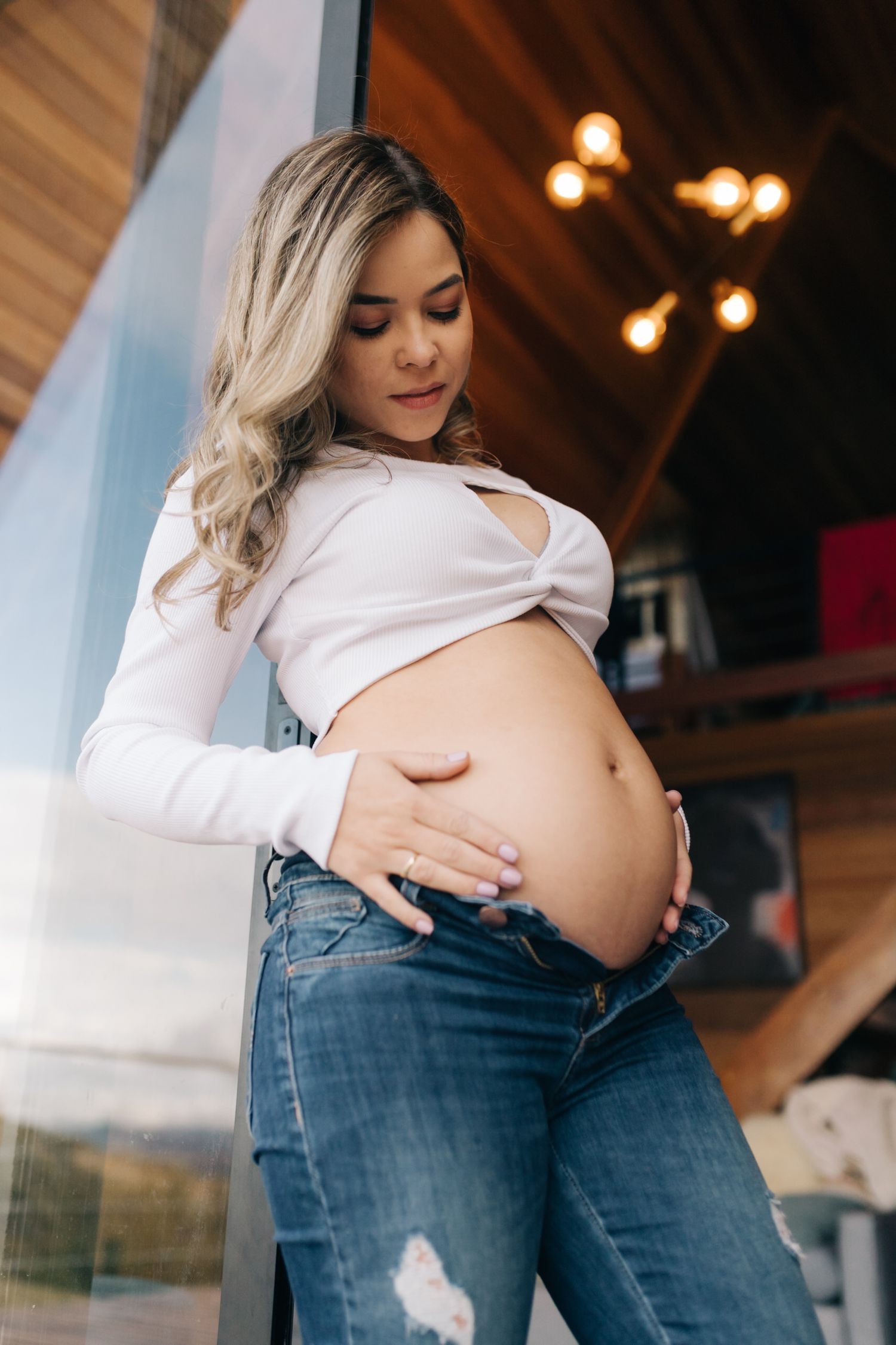 A maternity photo showing an expectant mother in white top and jeans against wooden interior.