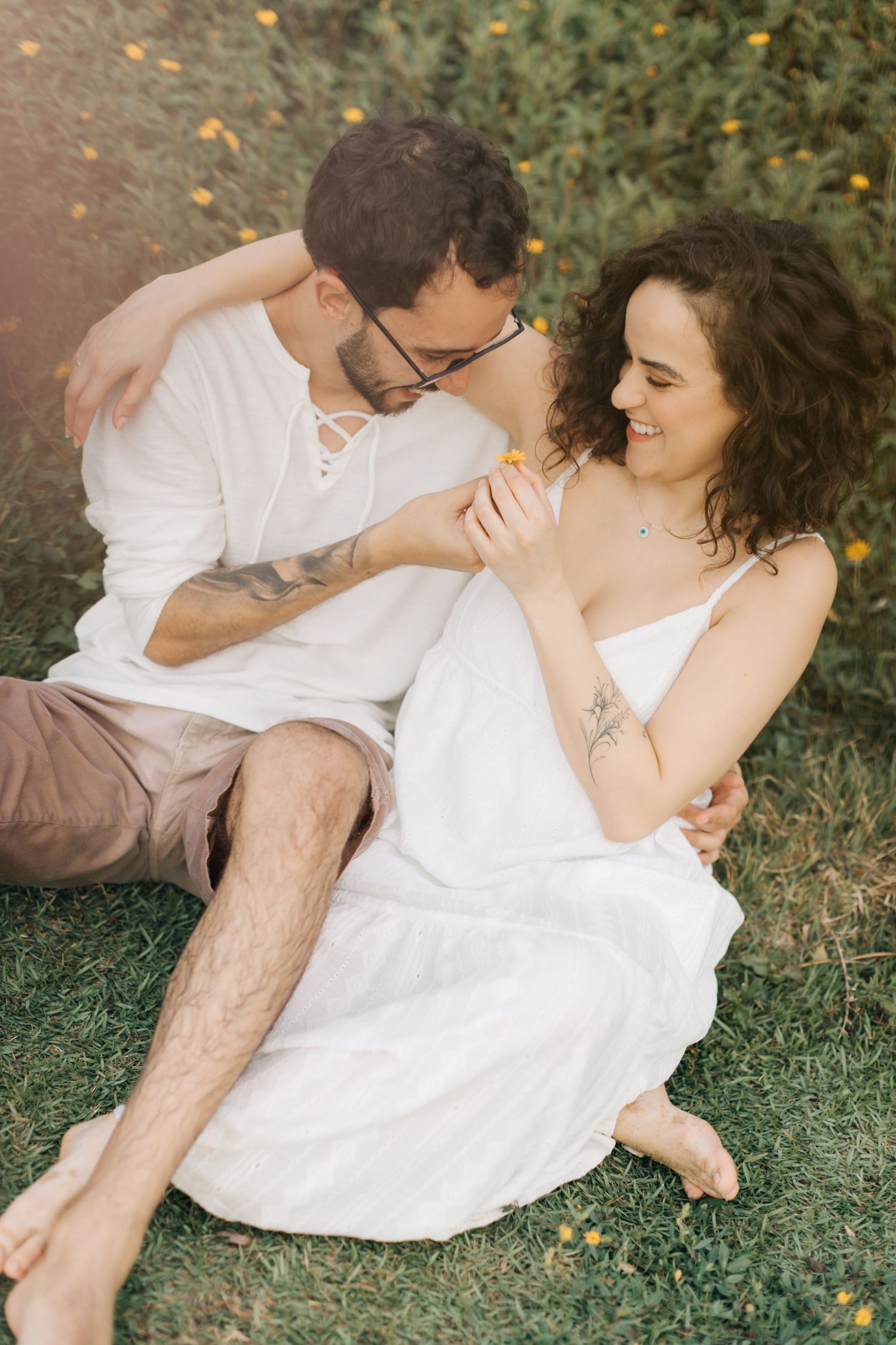 Intimate couple poses together on grass with yellow wildflowers in a romantic outdoor setting.