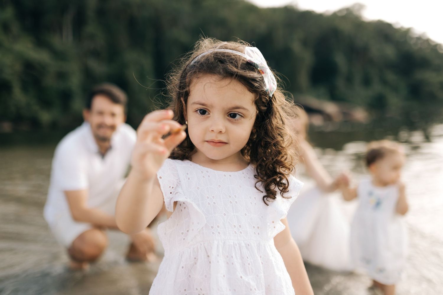 Child in white dress with curly hair during family beach photoshoot.