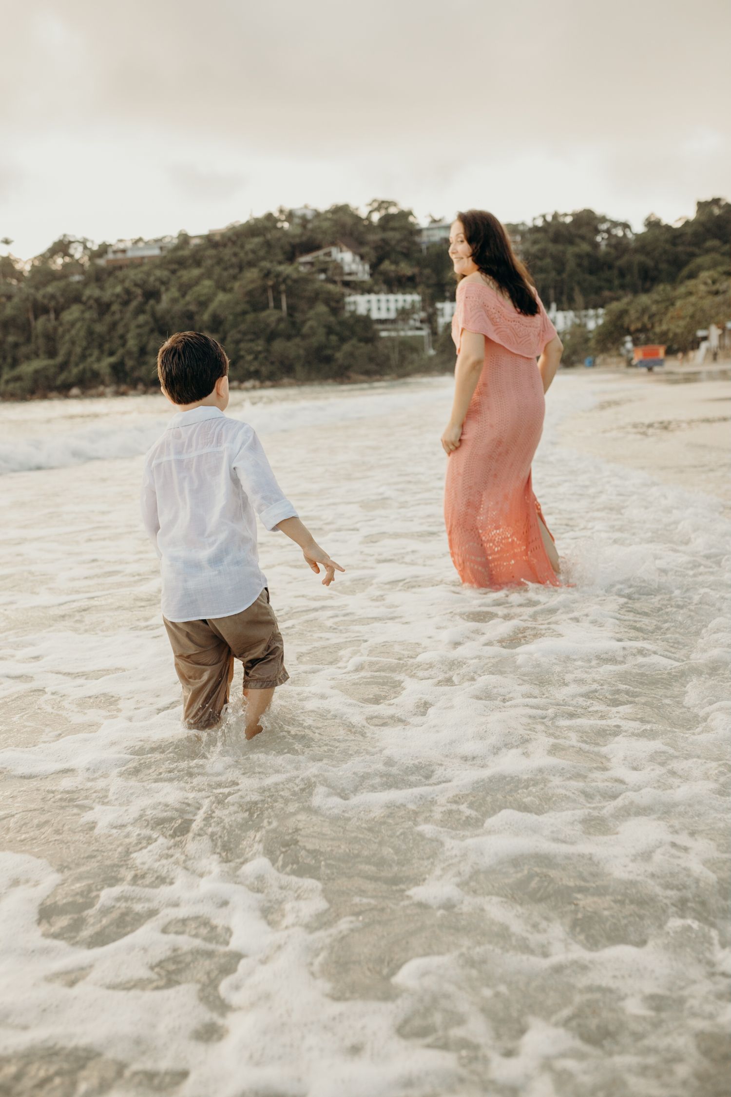 Two people wading through gentle ocean waves on a scenic beach.