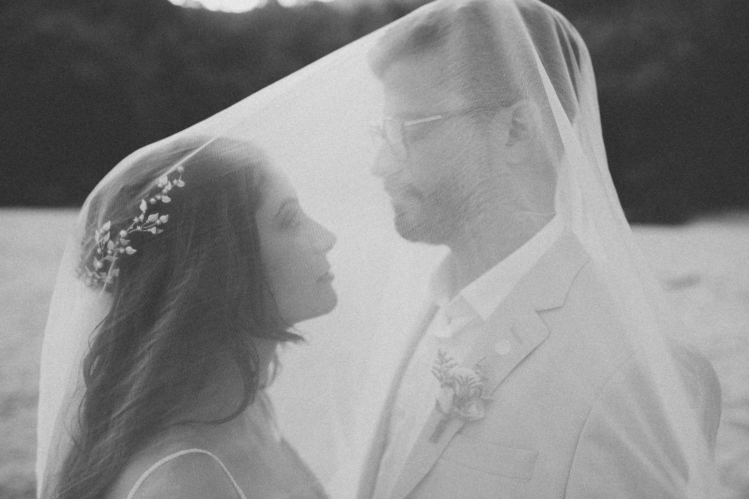 Monochrome wedding photograph capturing a romantic moment between newlyweds under a sheer veil.