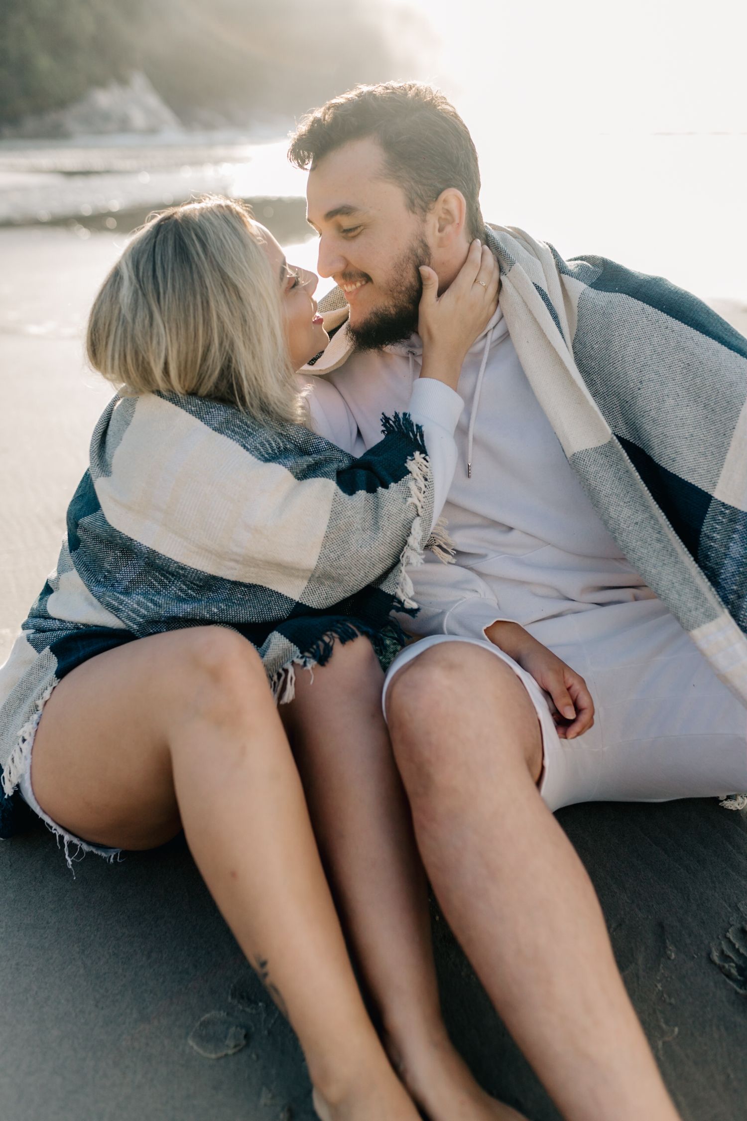 Tender beach moment captured with couple wrapped in striped blanket during sunset.
