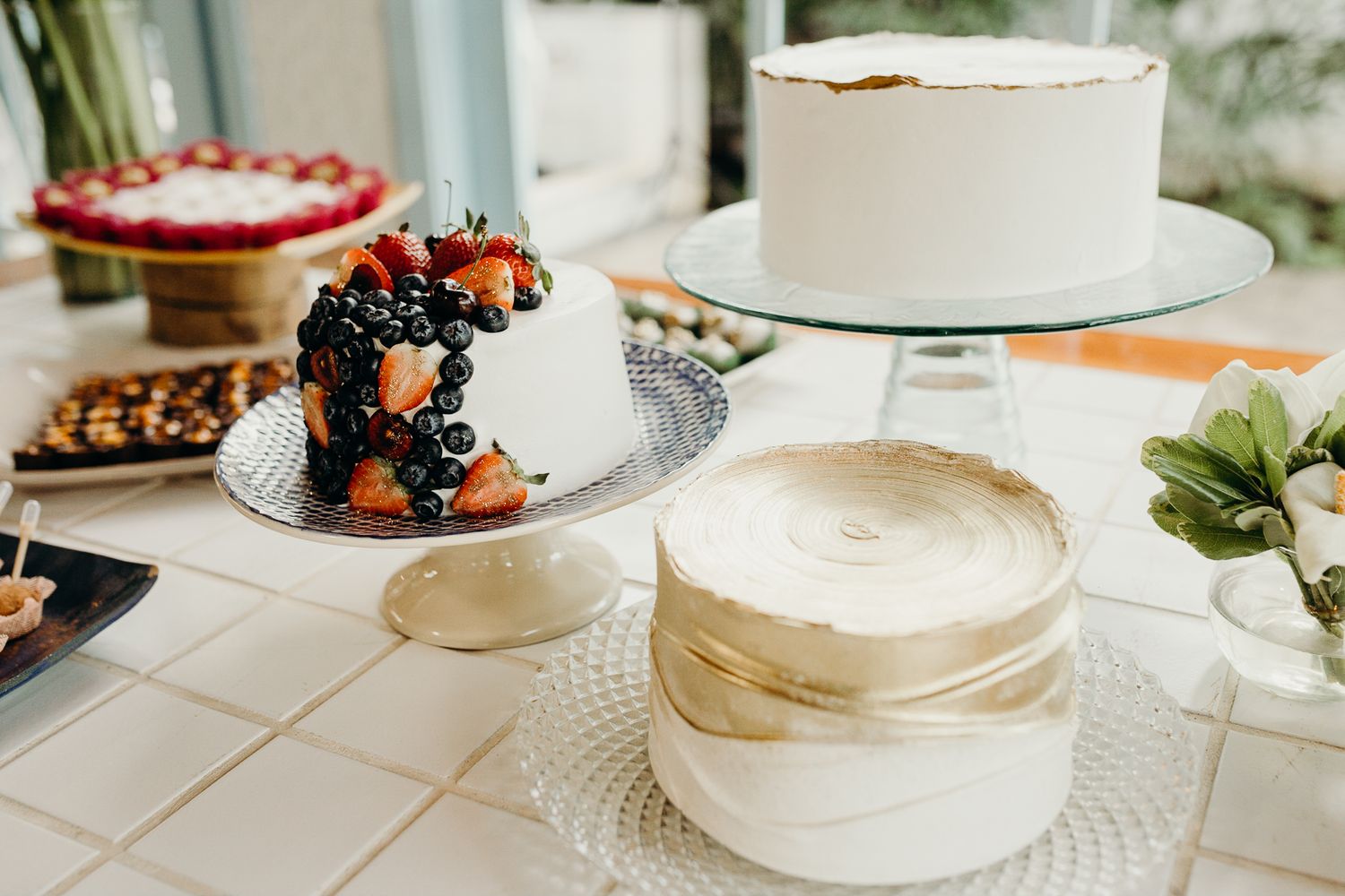 Elegant dessert display featuring white cakes and fresh berries on a white tablecloth.