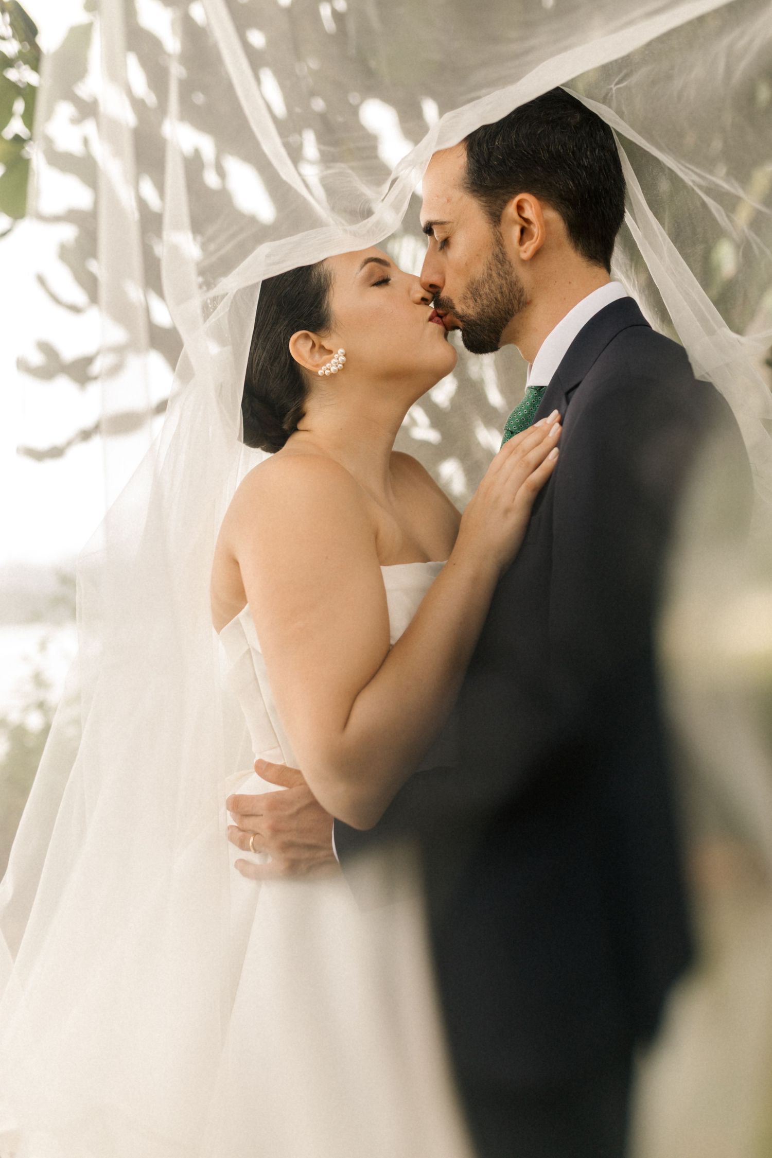Romantic newlyweds share a tender kiss under a flowing veil during their wedding ceremony.