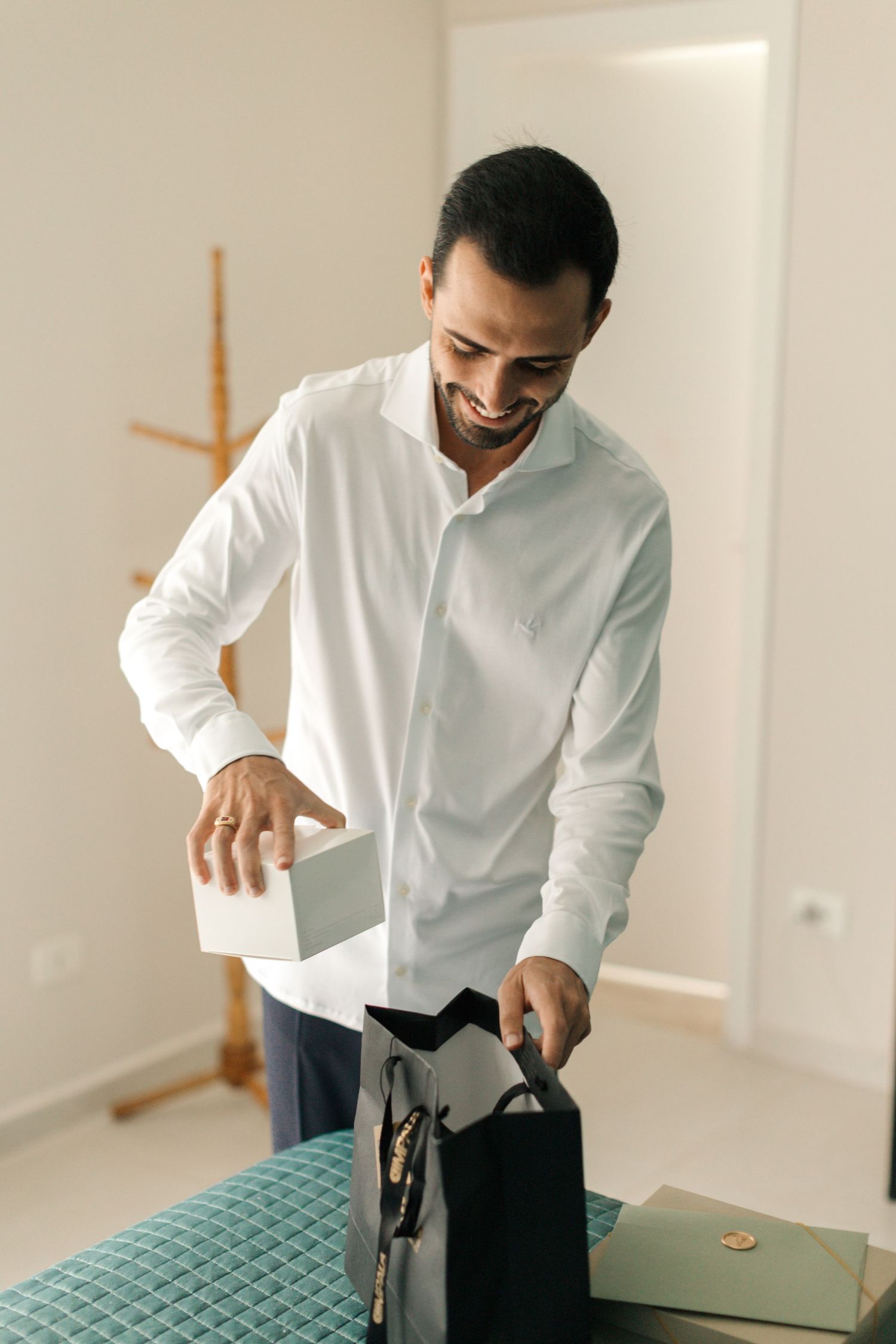 A person in white shirt smiles while opening a gift bag in an indoor setting.