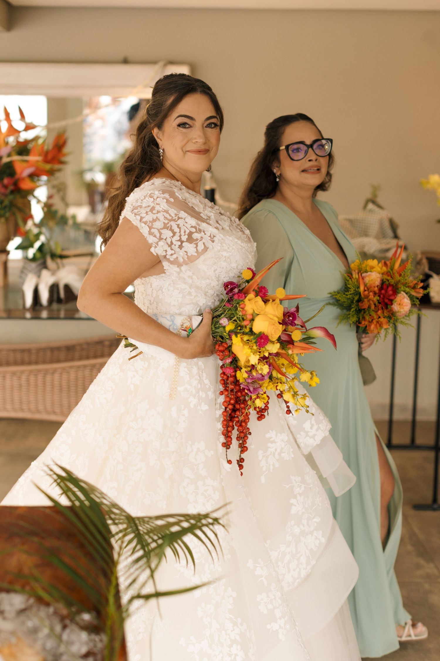 Wedding party members in mint green dresses holding vibrant orange and yellow bouquets.