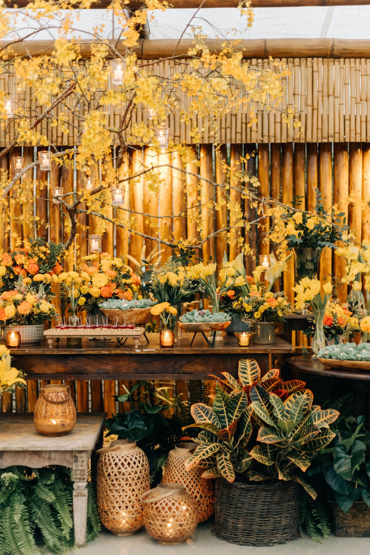 Rustic wedding decor with bamboo backdrop, yellow florals, and golden lanterns.