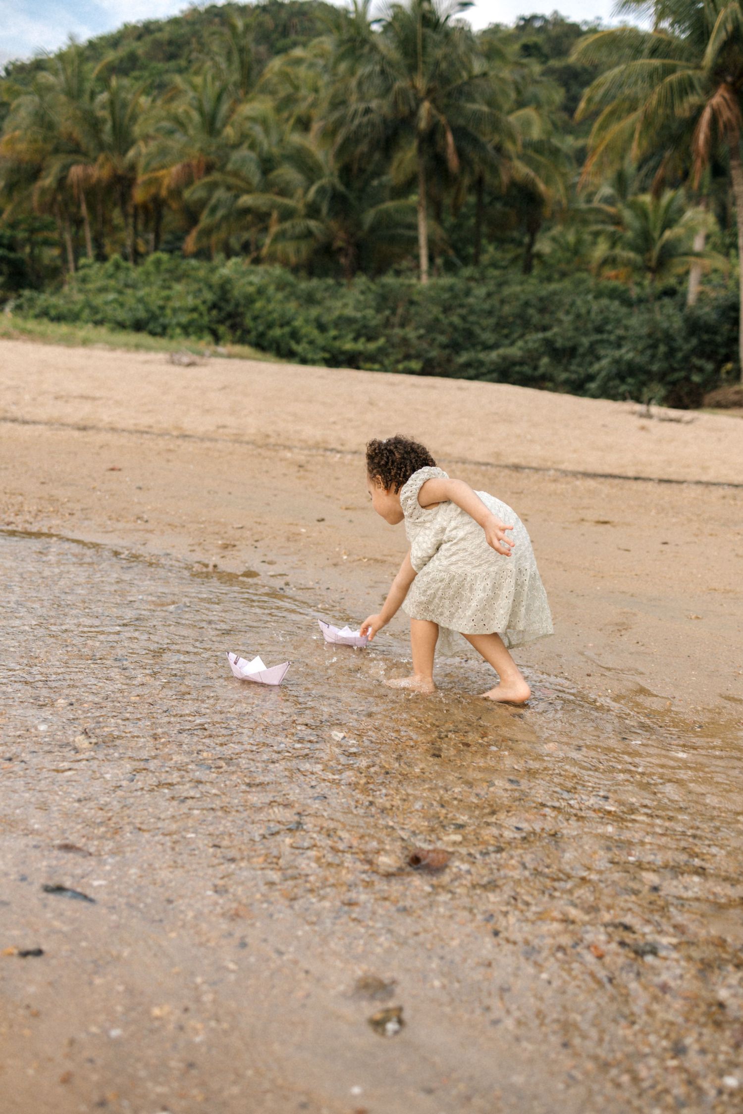 Person exploring and collecting items along a tropical beach with palm trees in the background.
