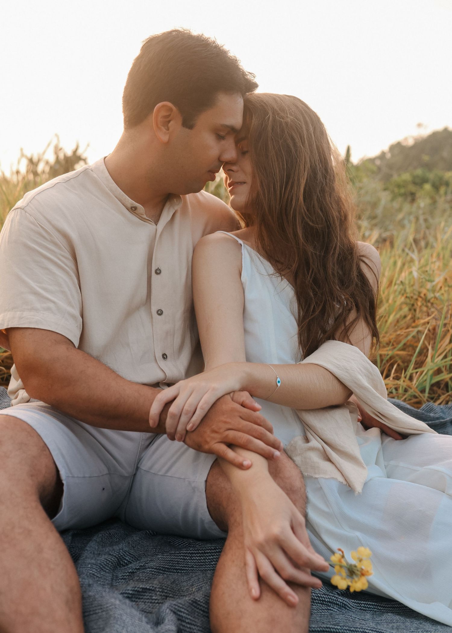 Couple in white outfits sharing intimate moments on picnic blanket outdoors.