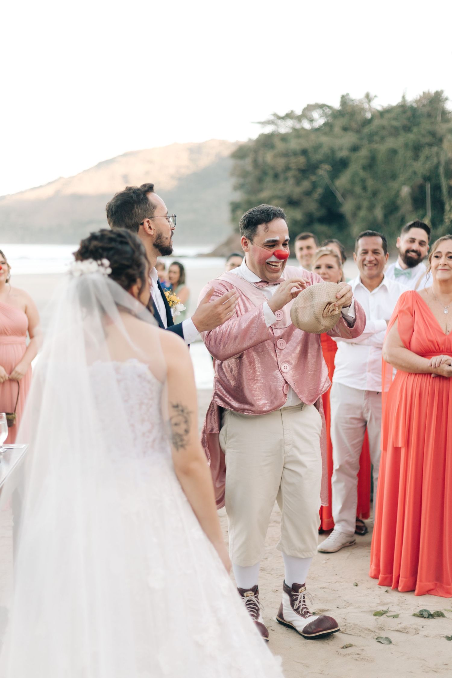 Wedding guest in pink shirt shows emotional response during beachside ceremony with guests looking on.