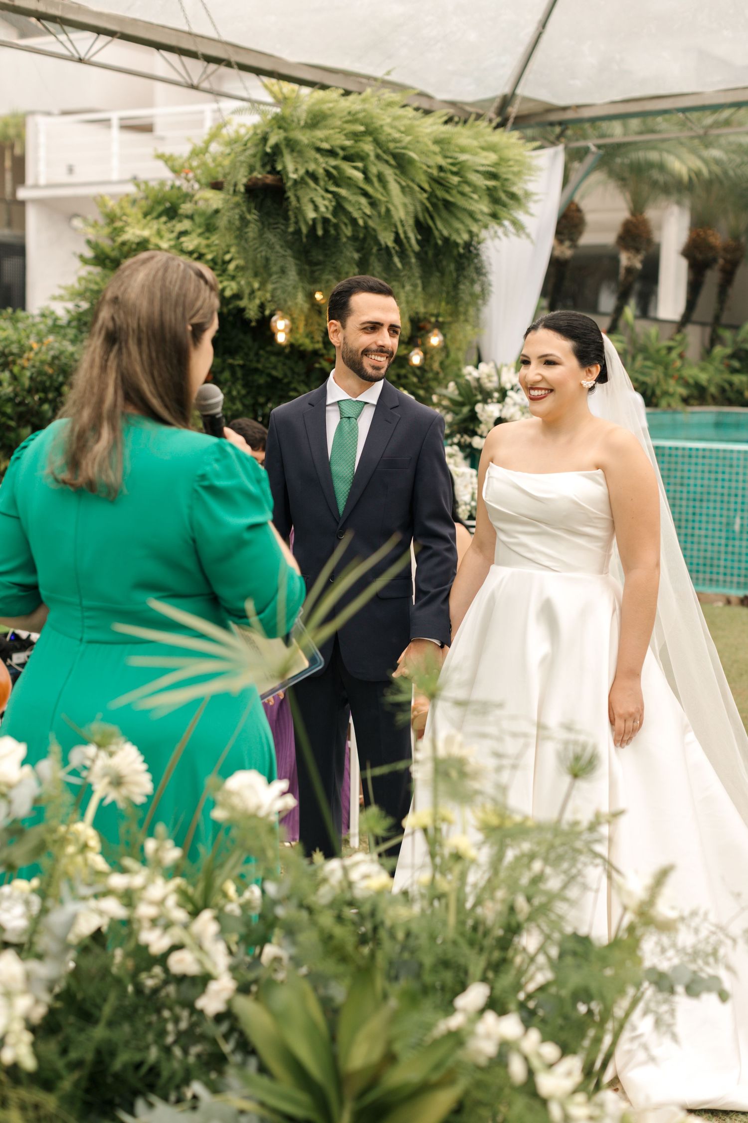 Outdoor wedding ceremony under white tent with lush greenery and floral decorations.