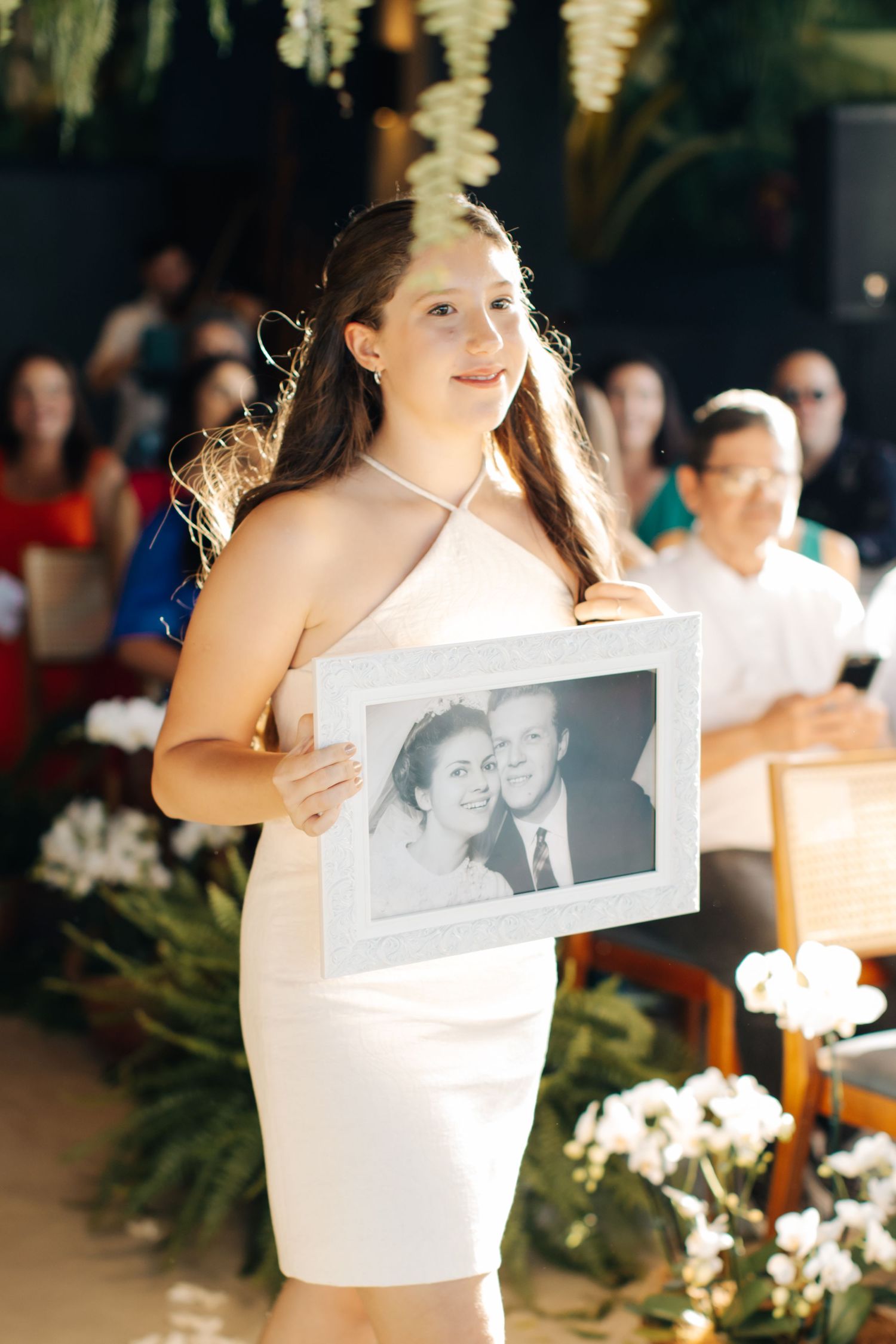 Person in white dress holding framed photograph during wedding celebration.