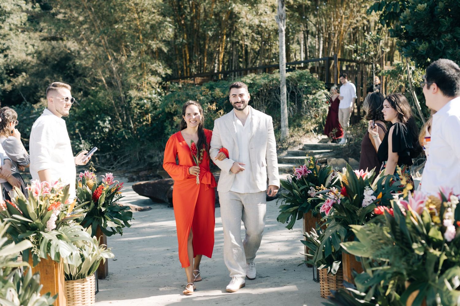 Guests socializing at an outdoor wedding reception decorated with tropical flowers.