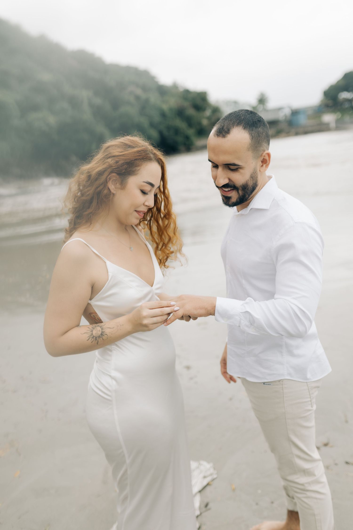 Couple examines engagement ring during romantic beach photoshoot.