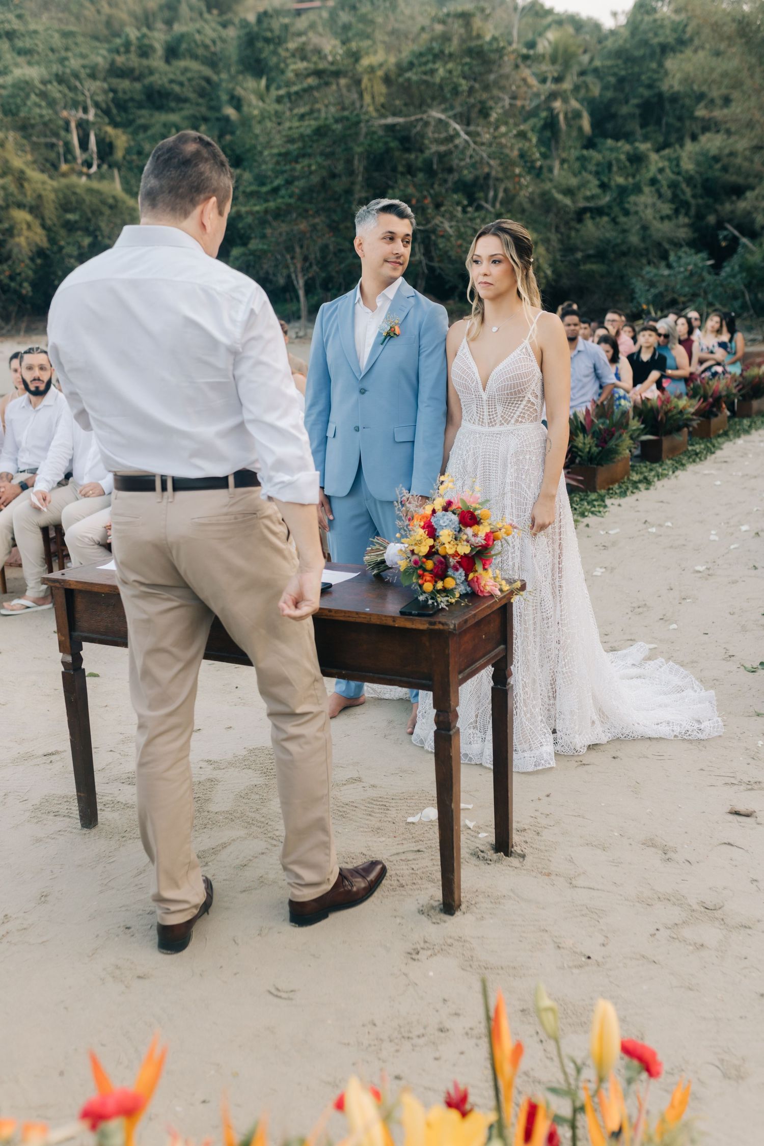 Outdoor beach wedding with wooden table and colorful floral arrangements.