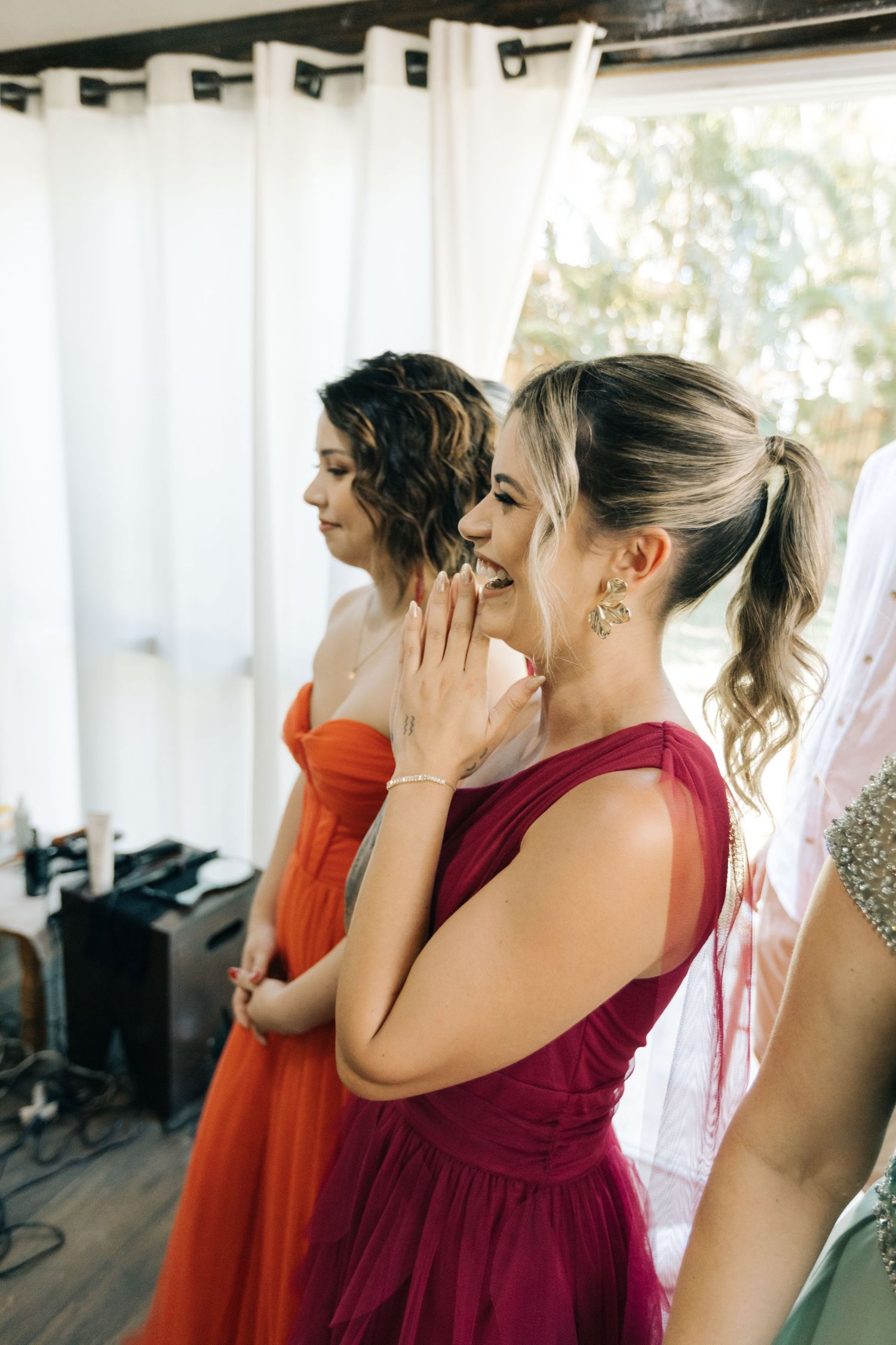 Wedding attendees in red and burgundy dresses share an emotional moment.