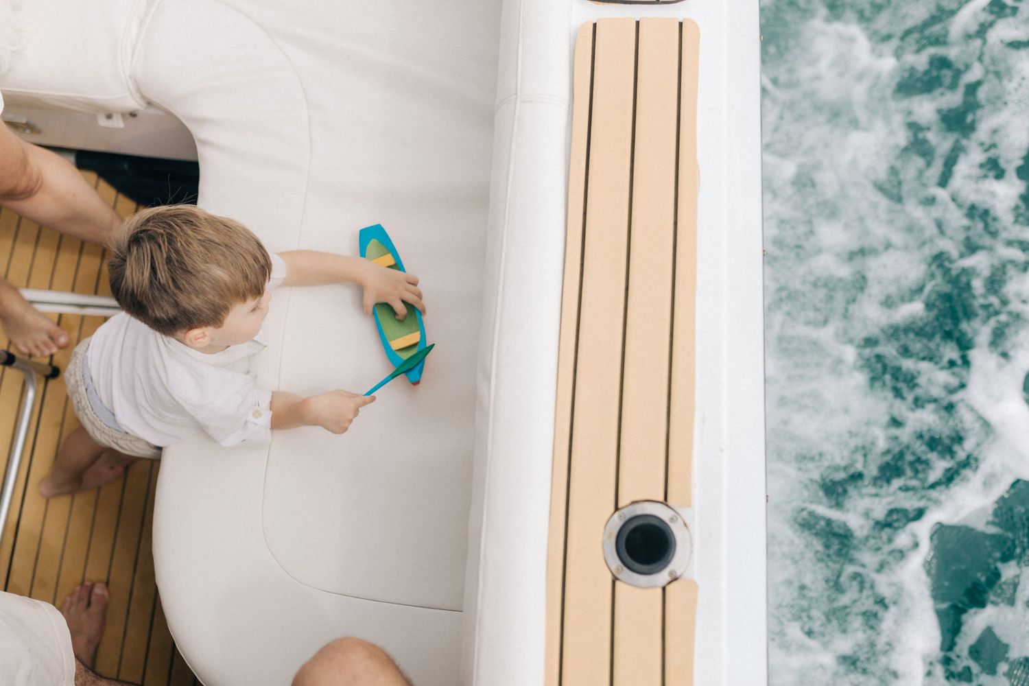 A small child in white plays on a bright surface near a window with ocean views.