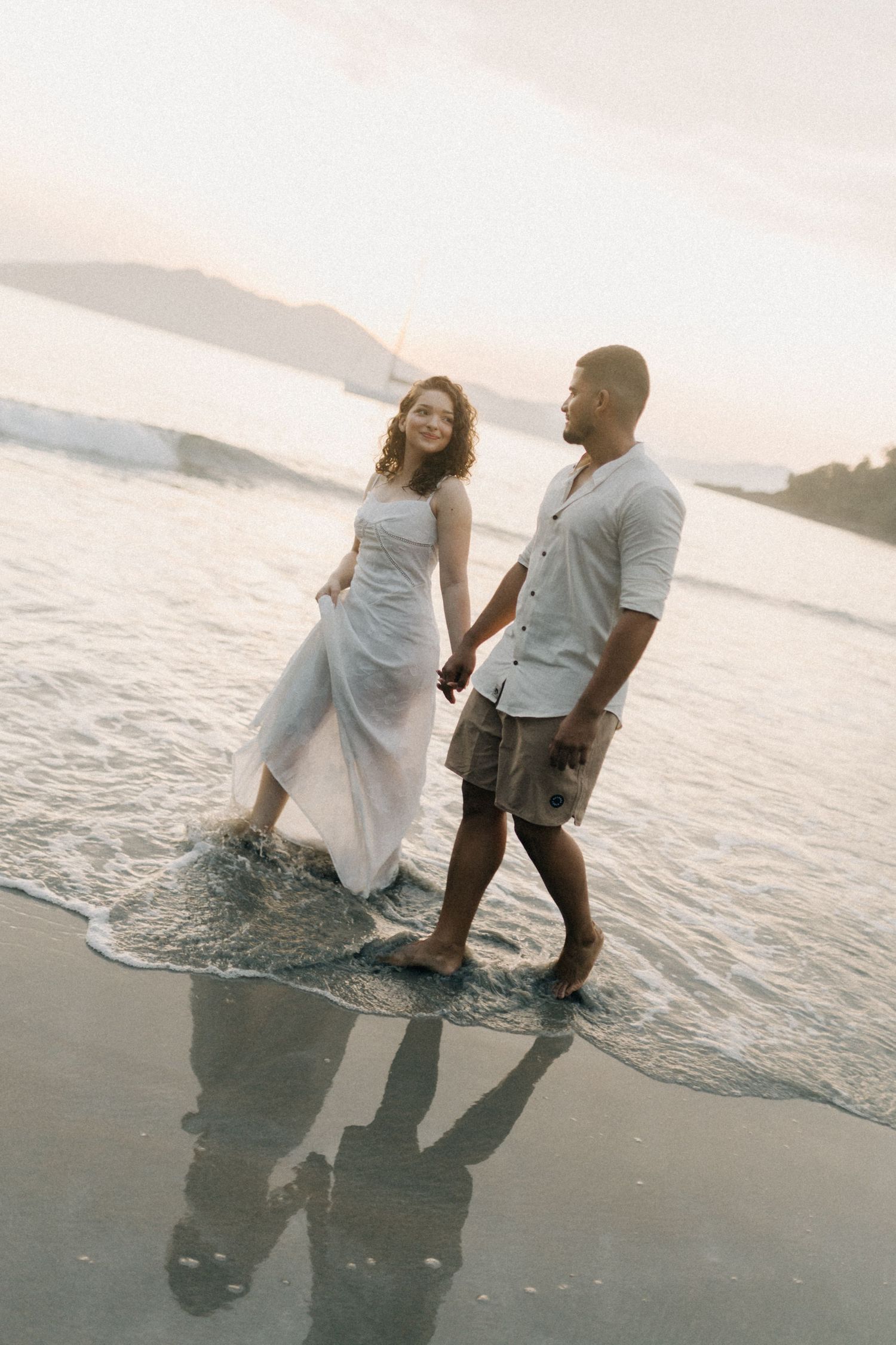 Two people playing and splashing in the shallow ocean waves at dusk.