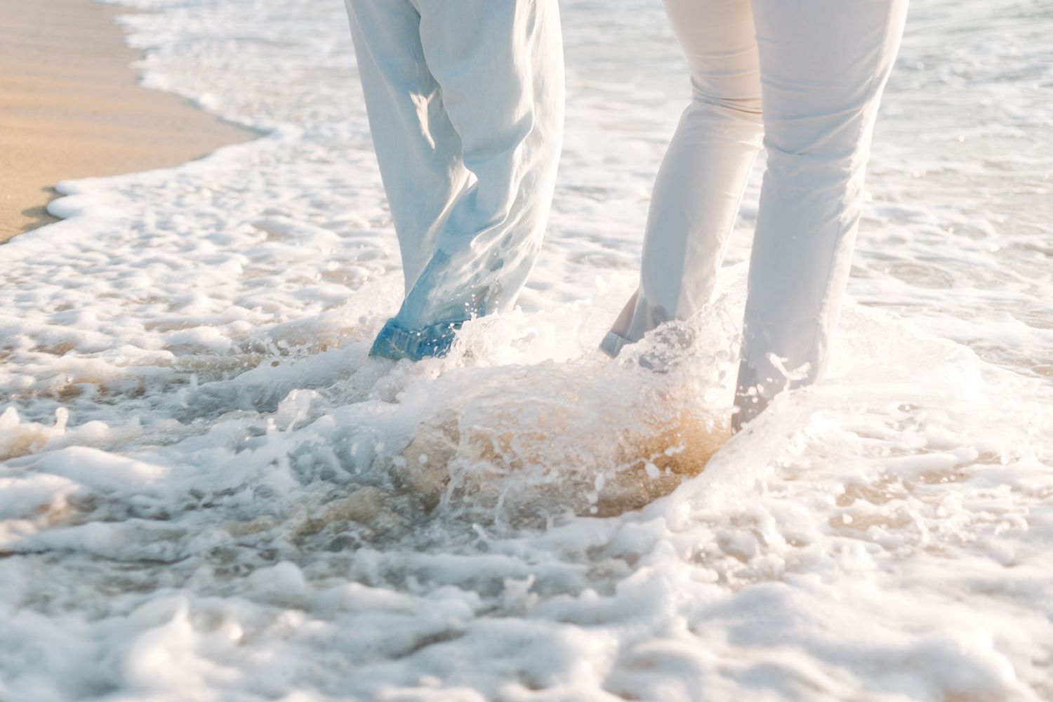 Feet splashing in ocean waves on beach during romantic photoshoot.