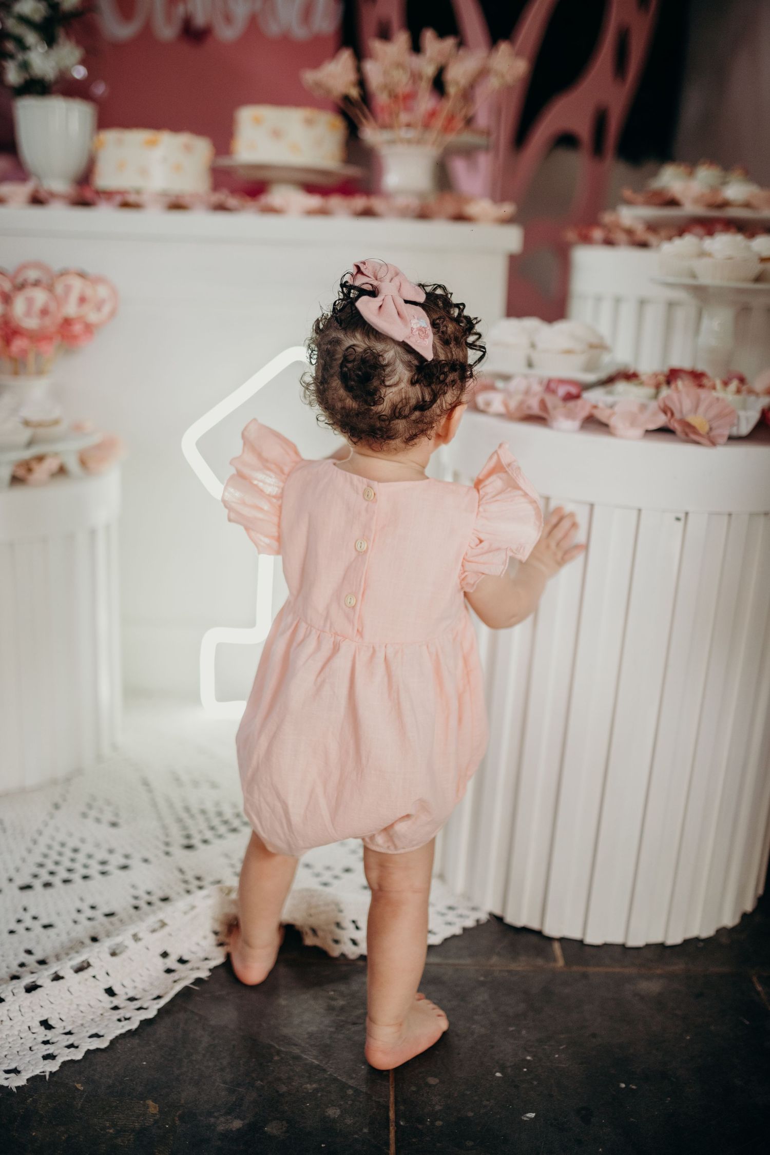 Baby in pink dress shown from behind near white decorative elements.