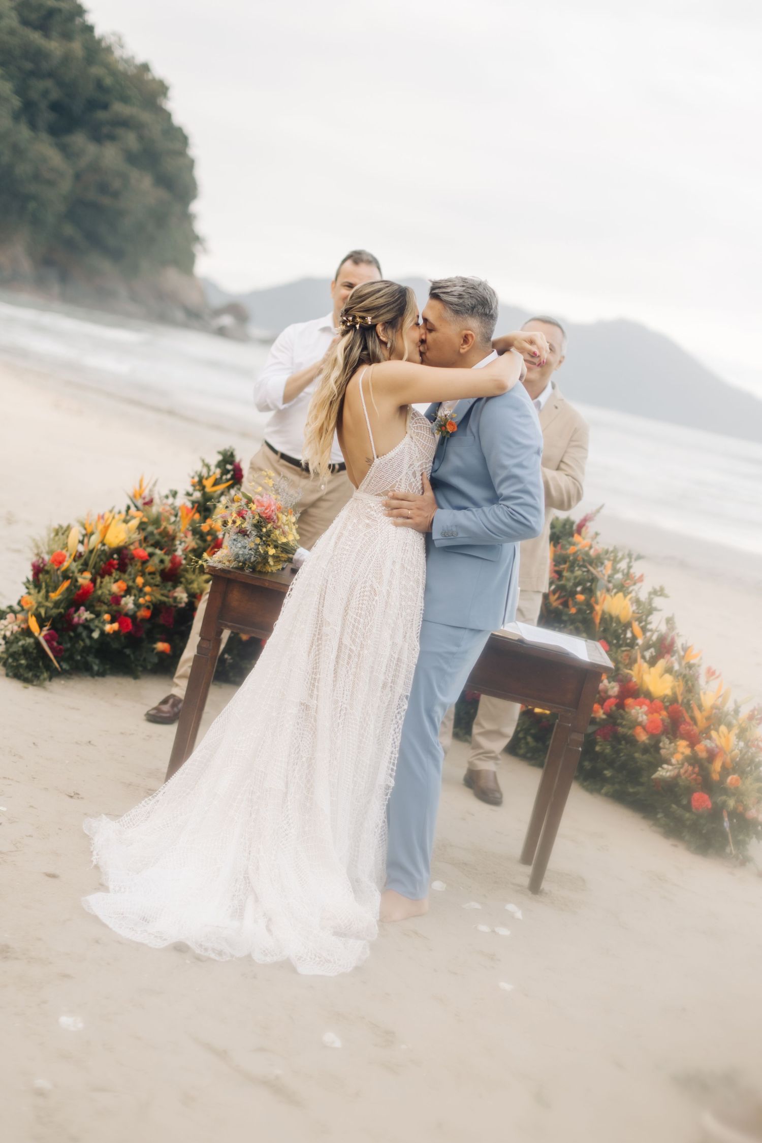 Newlyweds share an intimate dance moment on a beach with vibrant floral decorations.