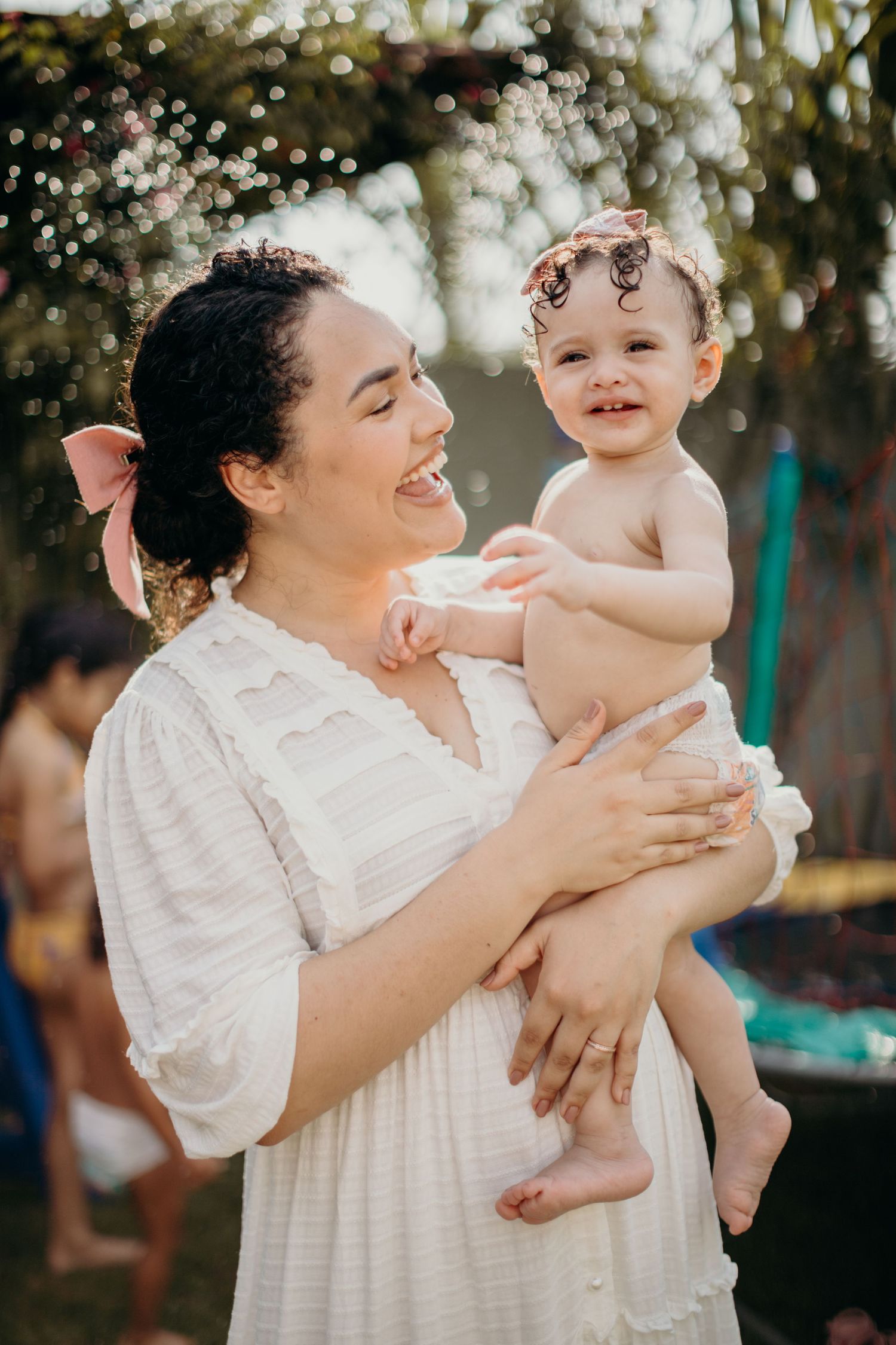 Joyful interactions between adult and baby wearing white outfits against a natural outdoor backdrop.