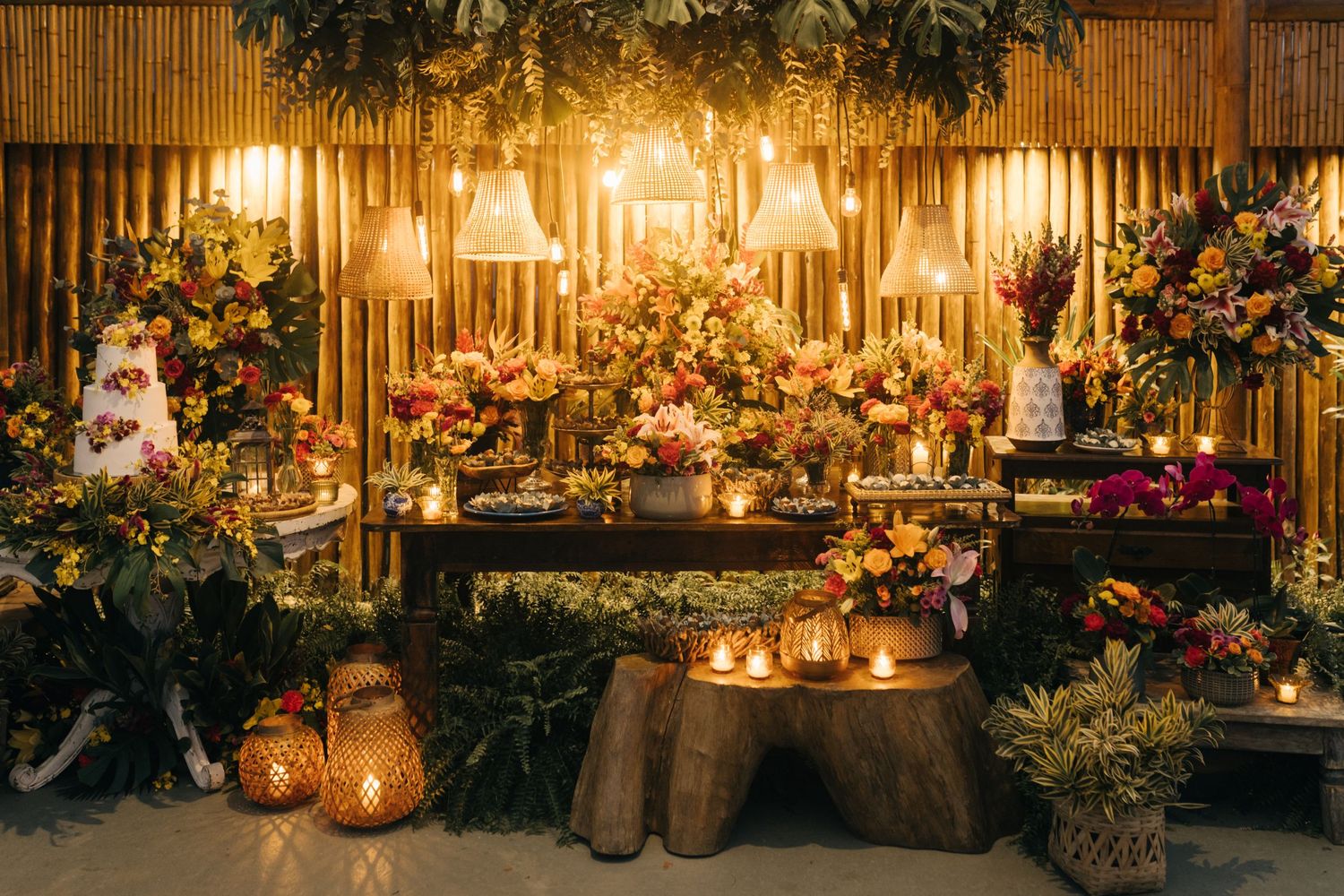 Elegant wedding reception setup with bamboo backdrop, lush greenery, and warm candlelit lanterns creating romantic ambiance.