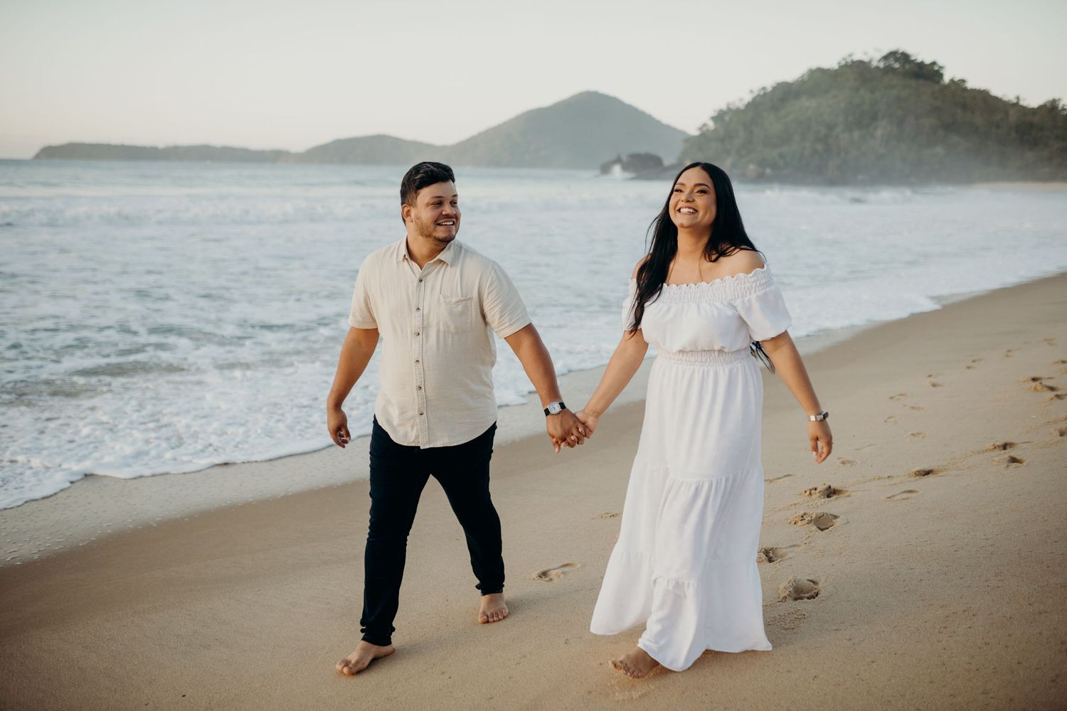 Happy couple walks hand in hand along the sandy shoreline.