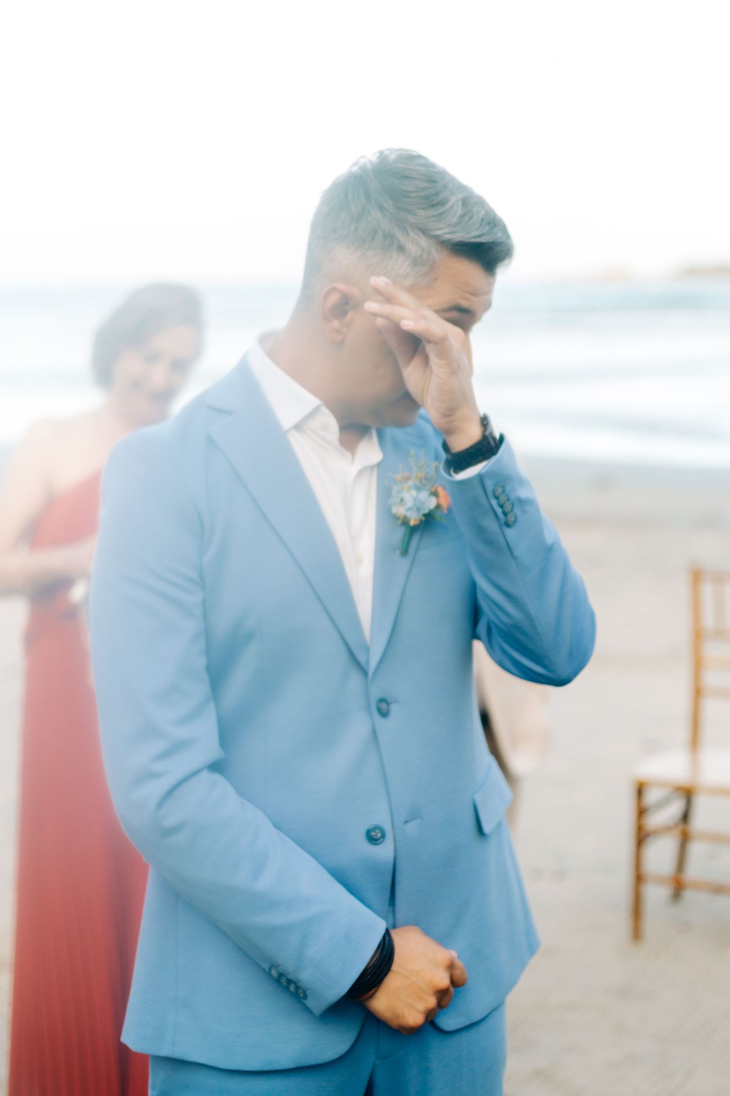 Emotional moment at beach wedding ceremony with light blue suit and ocean backdrop.