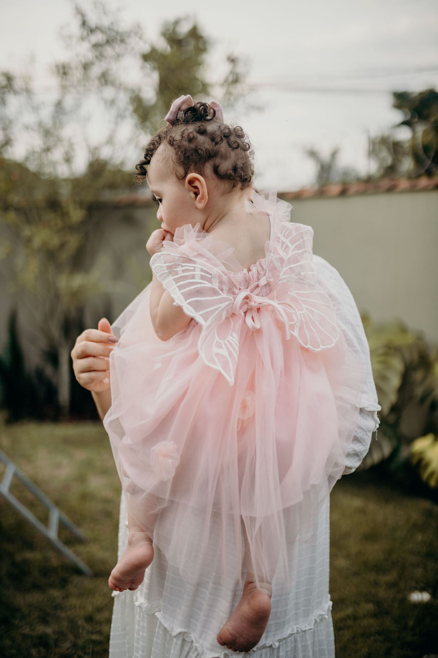 Tender moment with child wearing pink tulle dress with butterfly wings outdoors.