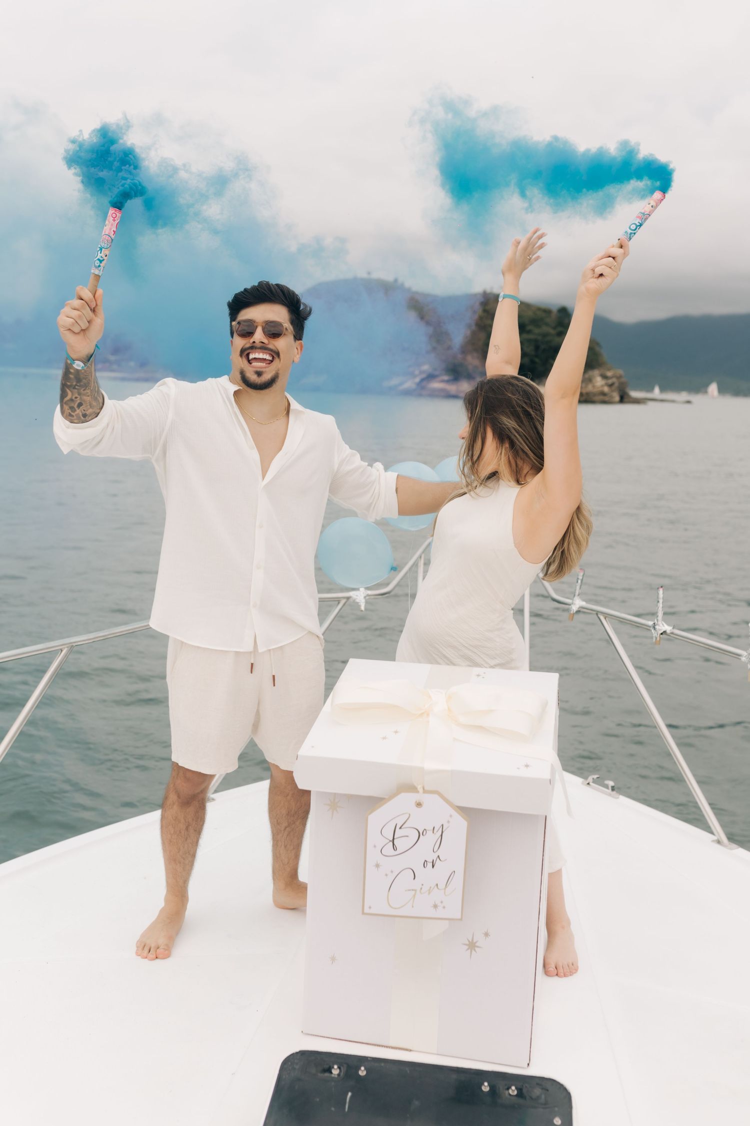Joyful celebration with blue smoke flares on white boat deck against coastal scenery.