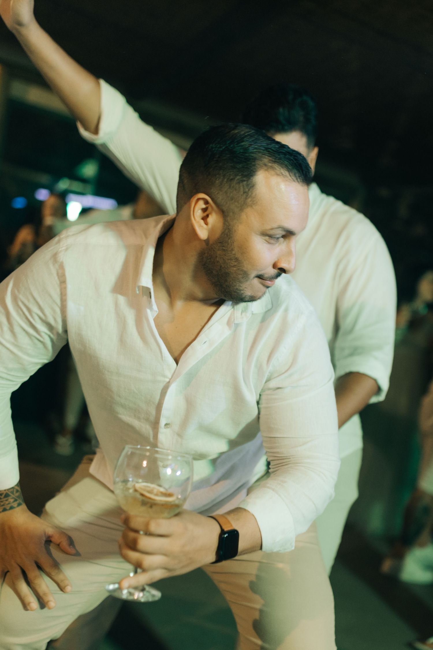 Wedding guest in white shirt dances while holding wine glass at indoor reception.
